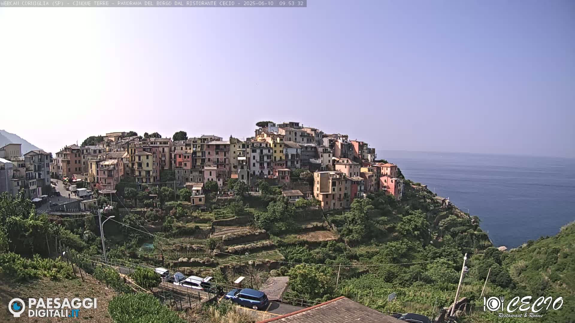 A colorful village clings to a hillside overlooking a calm ocean under a clear sky.