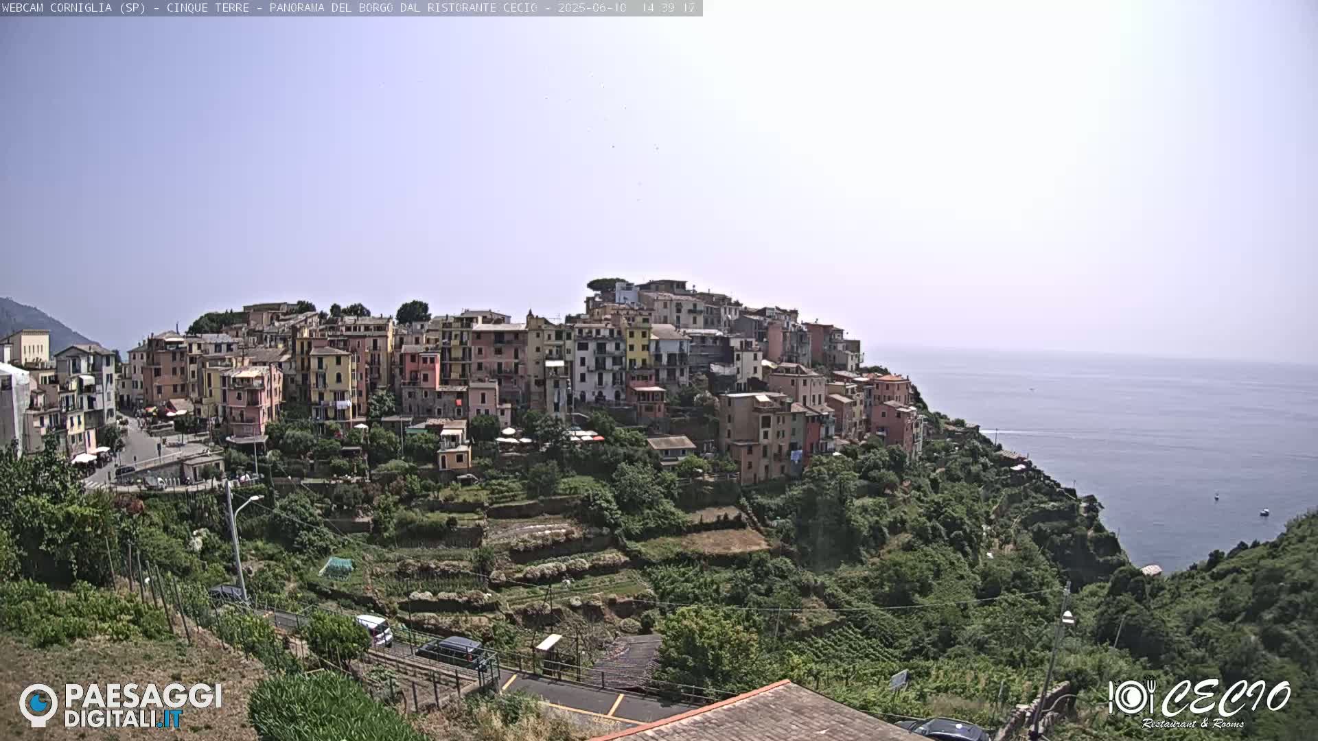 A hillside village of colorful buildings overlooks a calm ocean under a hazy sky.