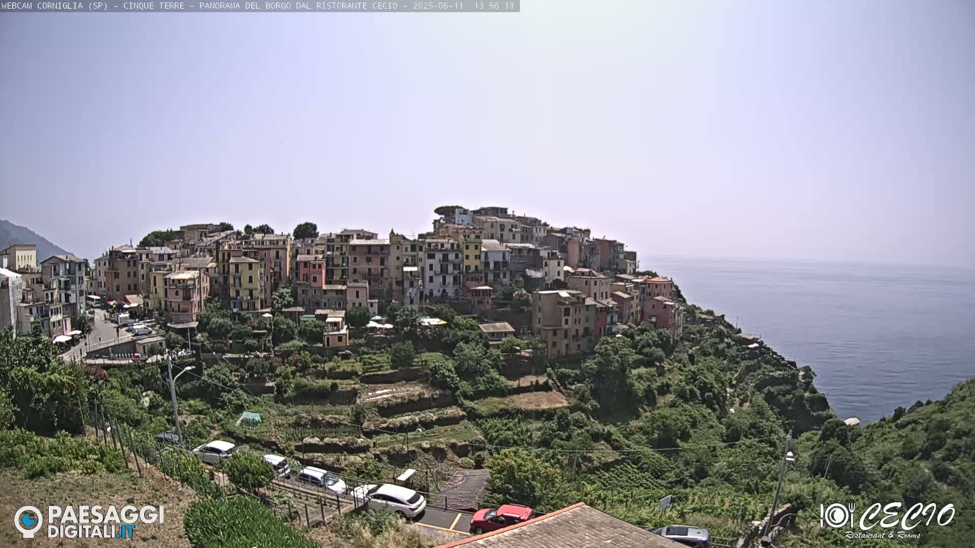 A colorful village clings to a hillside overlooking a calm, blue sea under a clear sky.
