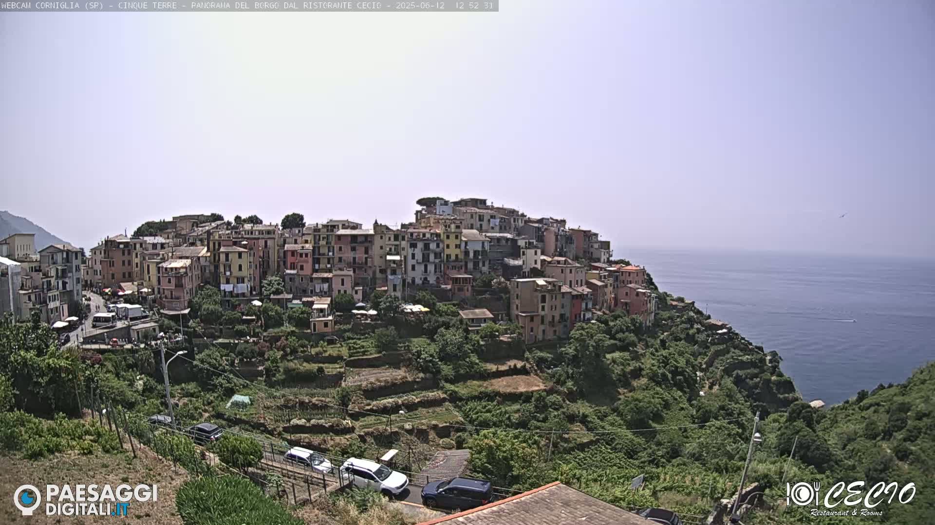 A hillside village of colorful buildings overlooks a calm blue sea under a clear sky.