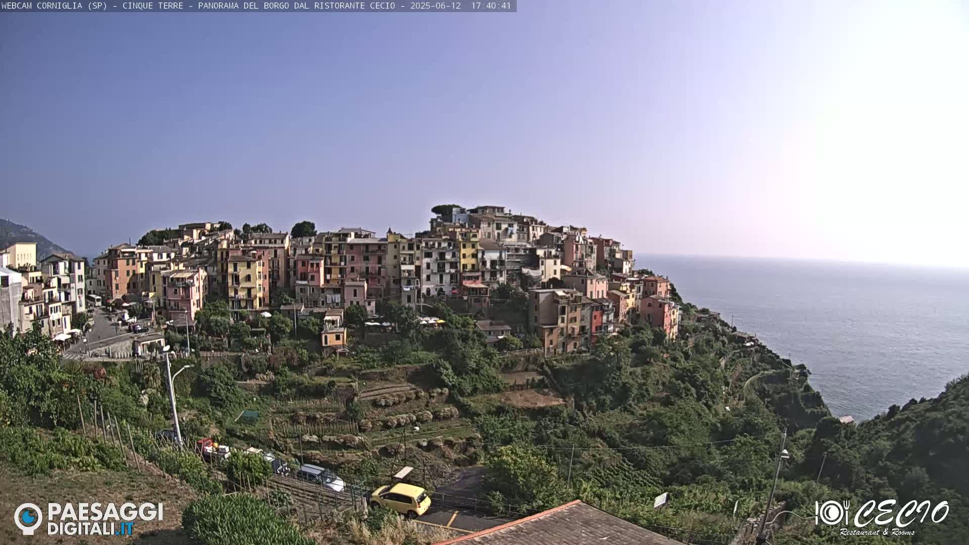 A colorful hillside village overlooks a calm ocean under a clear sky.