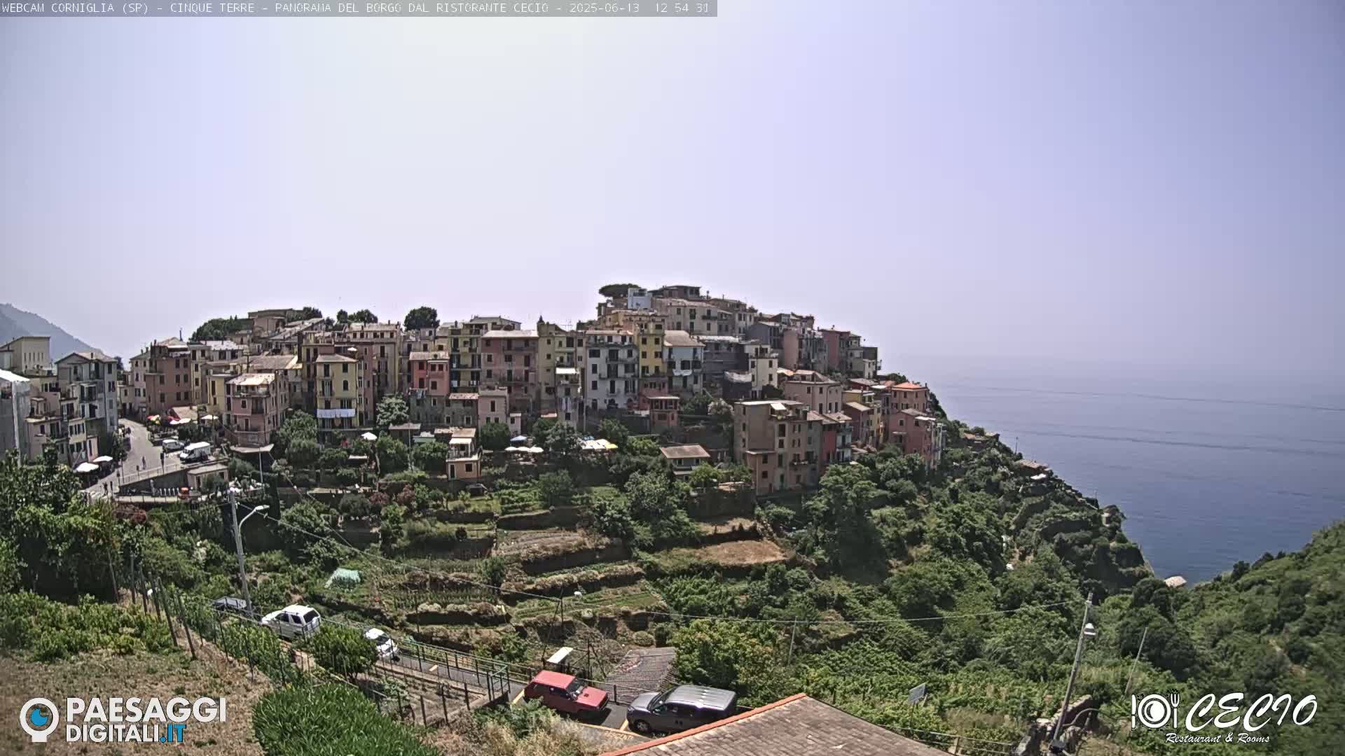 A colorful village clings to a hillside overlooking a calm ocean under a clear sky.