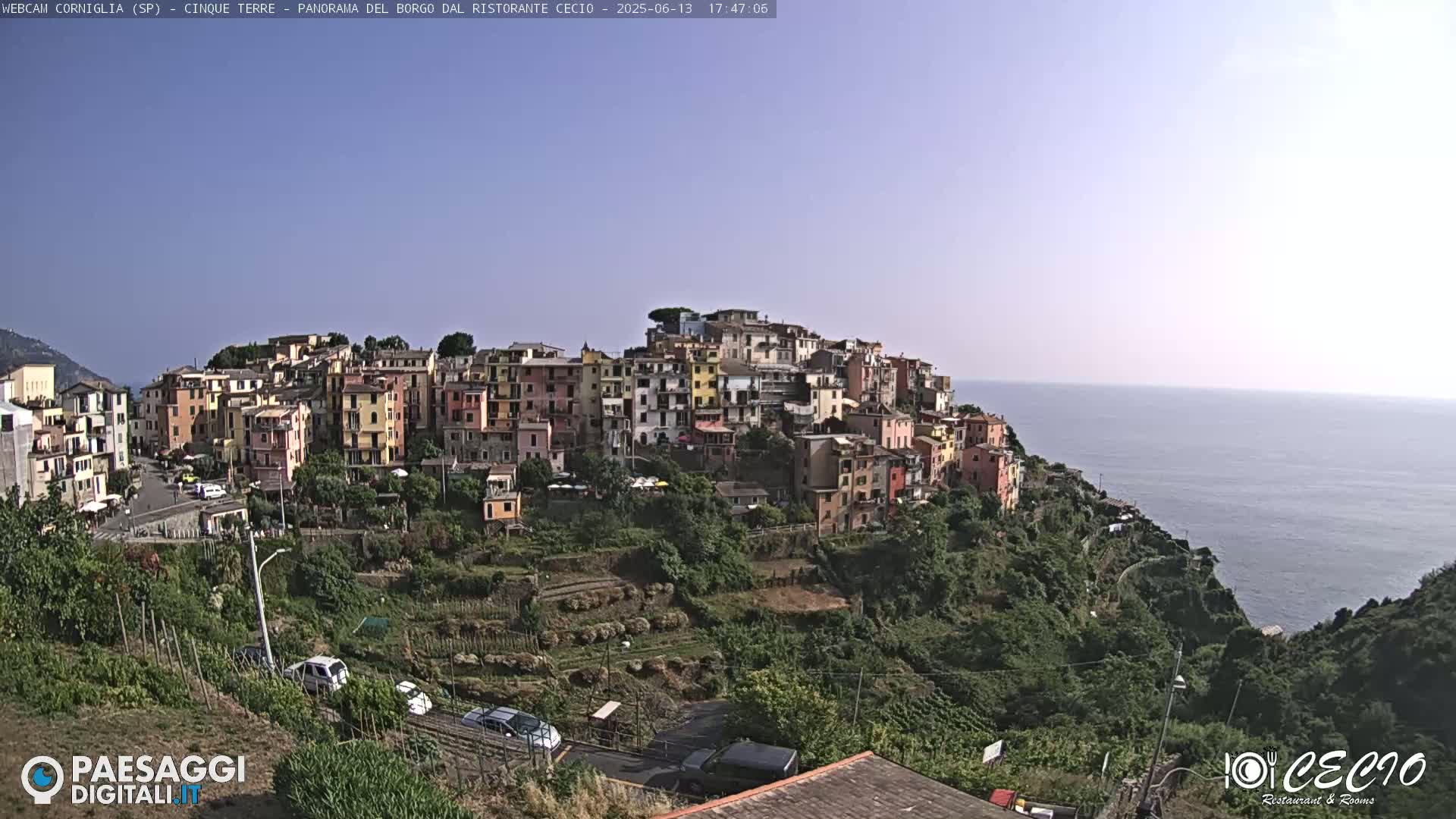 A colorful village clings to a hillside overlooking a calm sea under a clear sky.