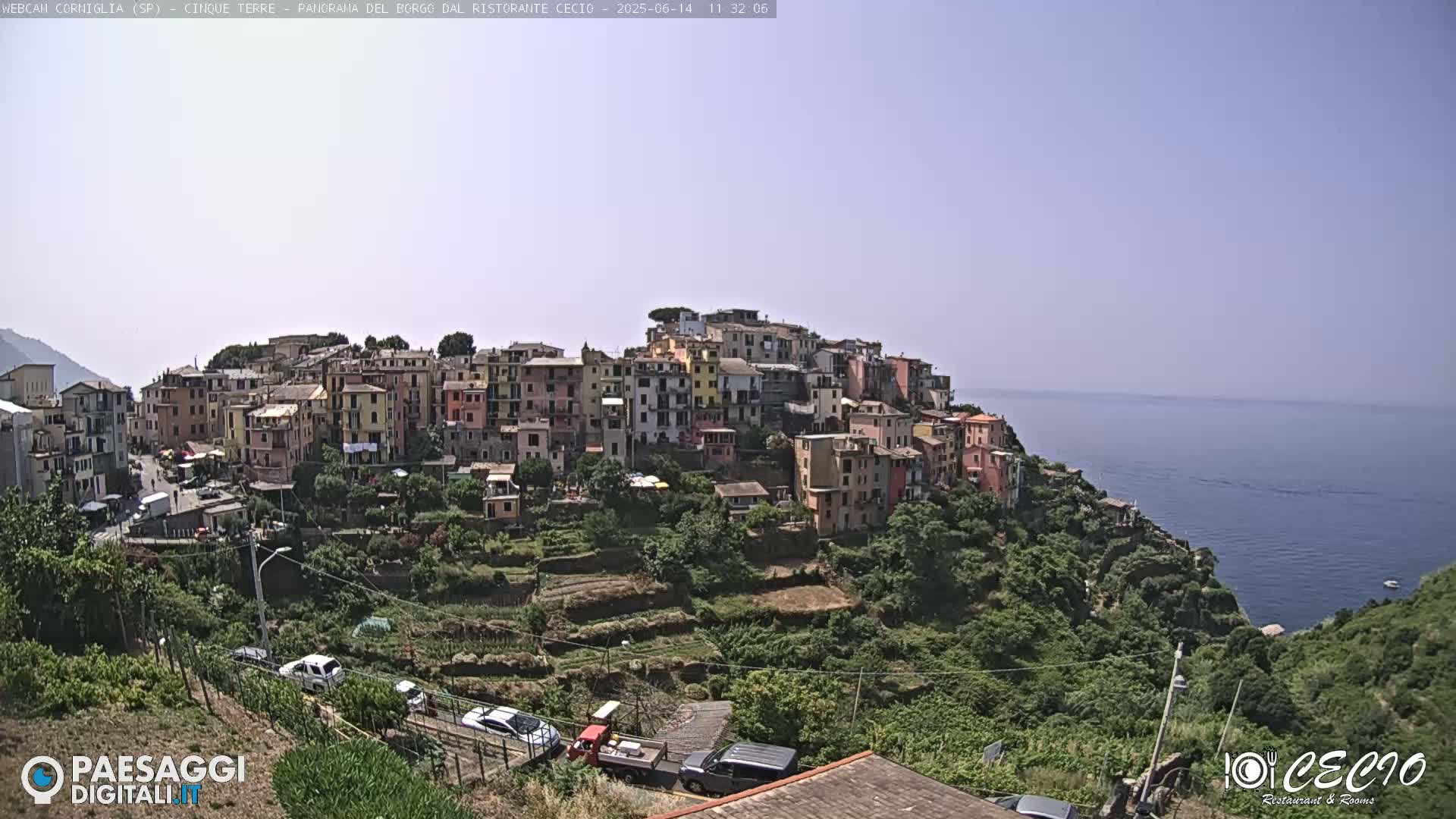 A colorful hillside village overlooks a calm ocean under a clear, bright sky.