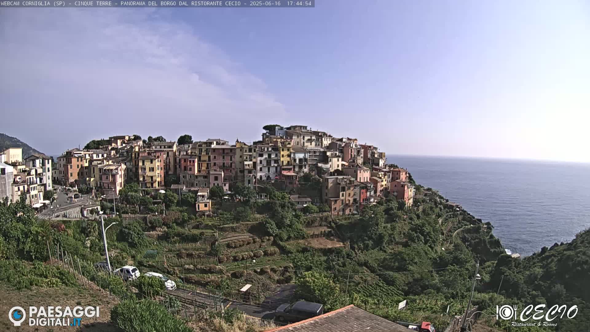 A colorful hillside village overlooks a calm ocean under a mostly clear sky.