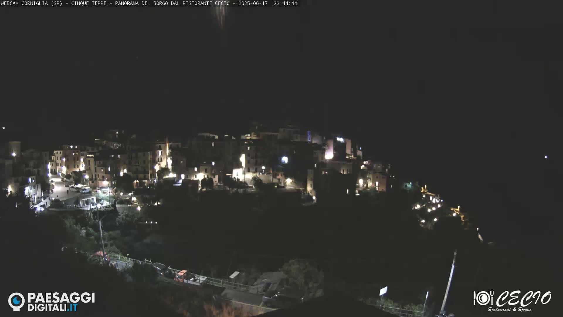 A nighttime, aerial view of a small, hilltop town with illuminated buildings under a clear, dark sky.