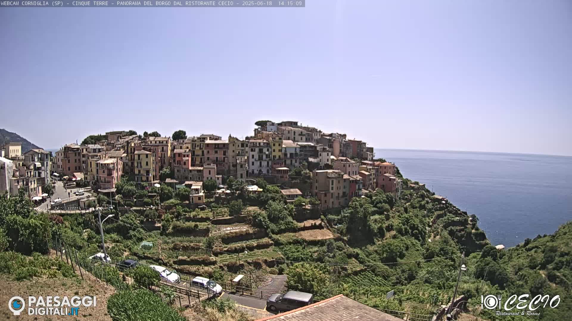 A colorful hillside village overlooks a calm ocean under a clear sky.