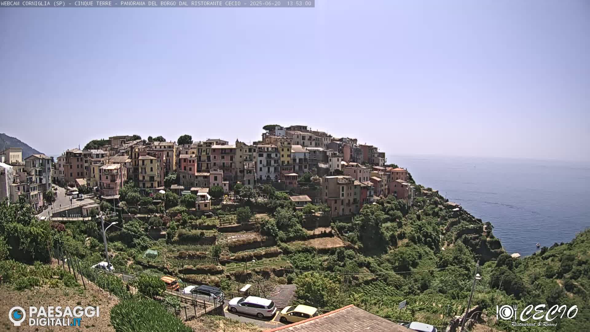 A coastal village of colorful buildings clings to a hillside overlooking a calm blue sea under a clear sky.