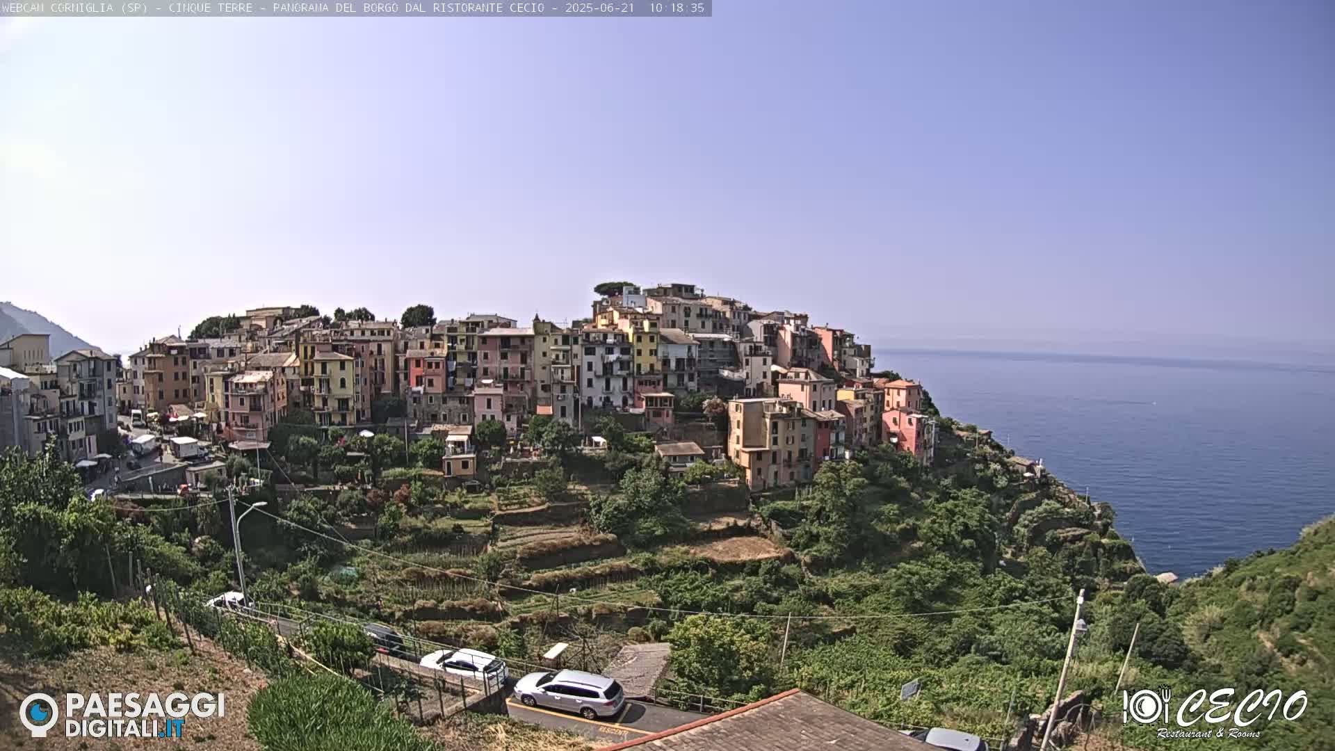 A colorful village clings to a hillside overlooking a calm blue sea under a clear sky.