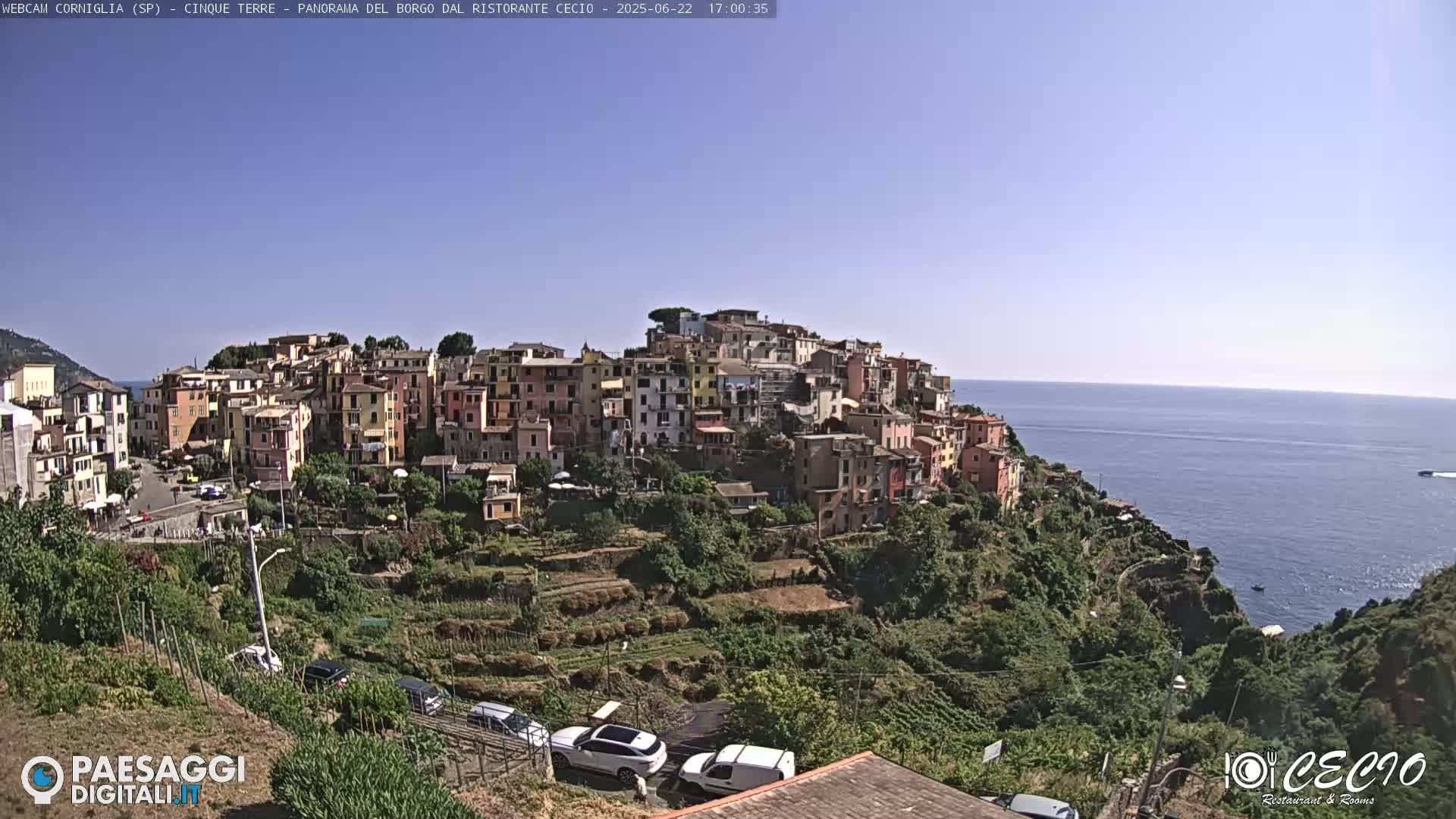 A colorful hillside village overlooks a calm blue sea under a clear sky.