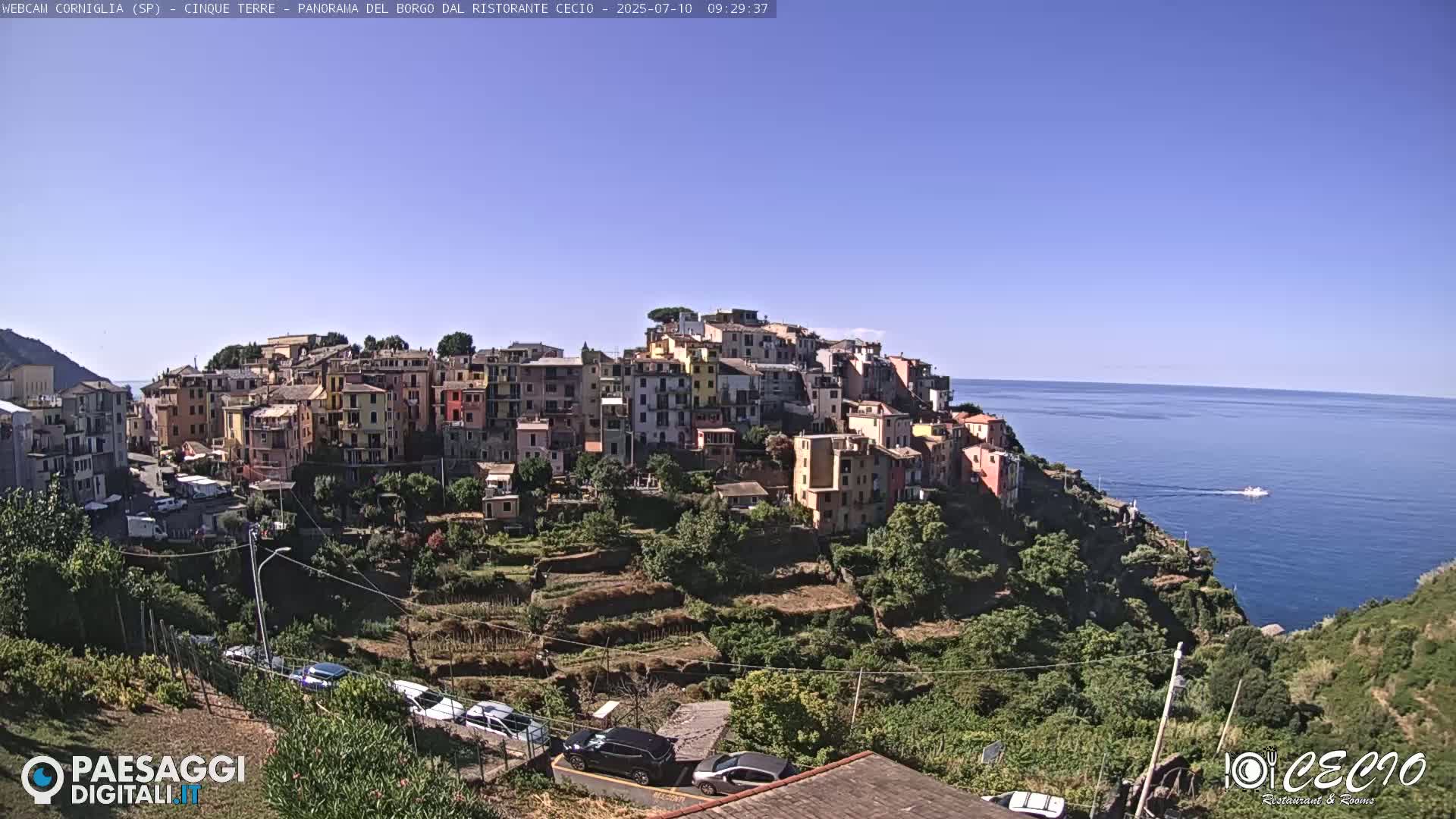 A colorful hillside village overlooks a calm blue sea on a clear, sunny day.