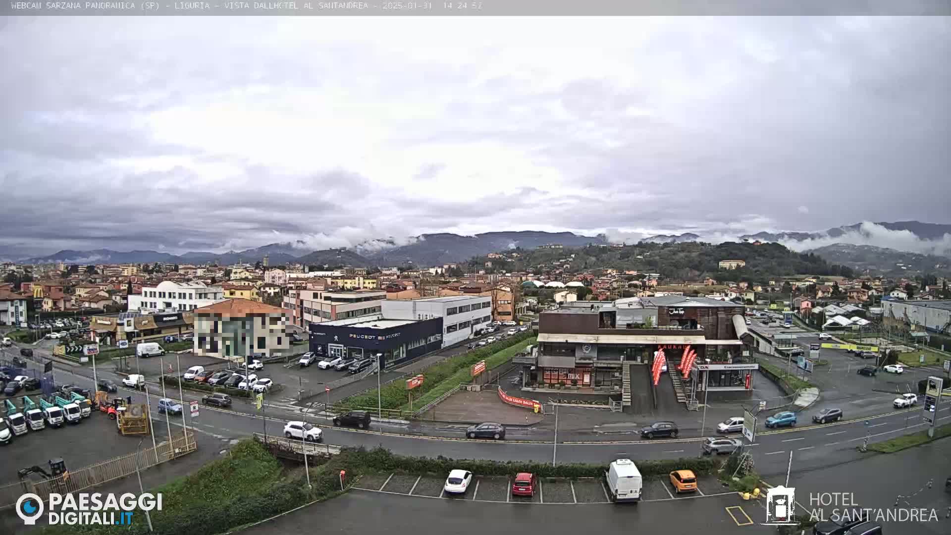 A sprawling town scene under a cloudy sky, showing numerous buildings, parked cars, and a busy roadway.