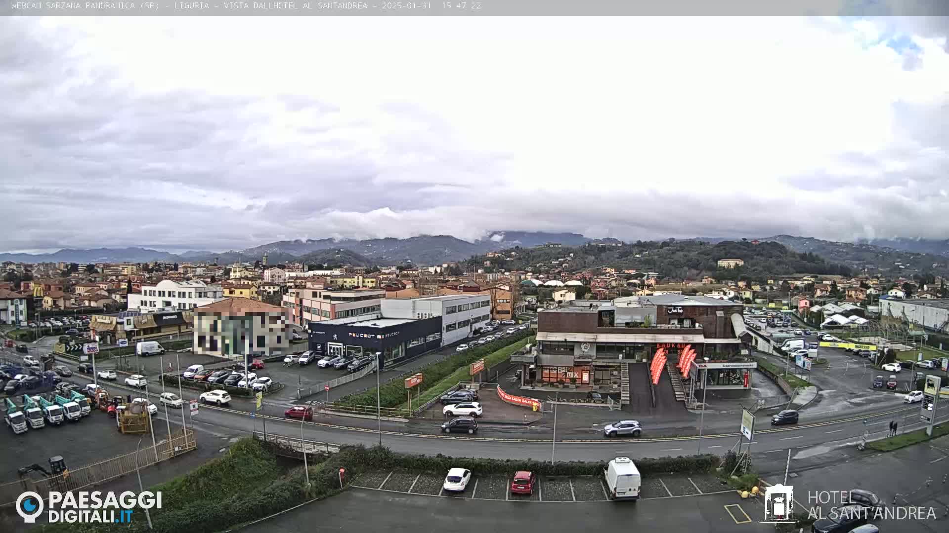 A cloudy day overlooking a town with buildings, parking lots, and vehicles, and distant mountains in the background.