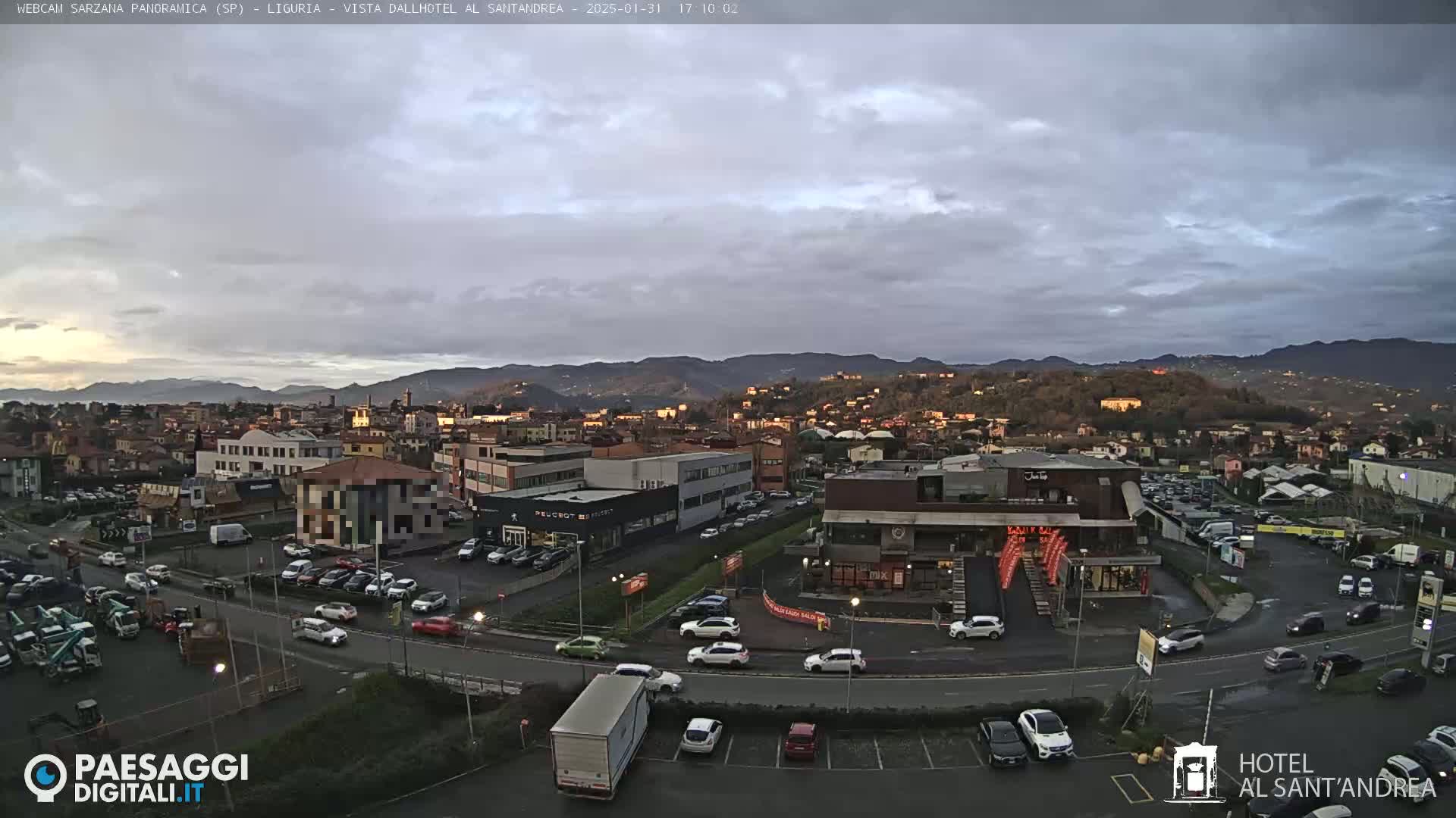 An overcast sky hangs over a town nestled in a valley, with cars parked in lots surrounding various buildings near a roadway.