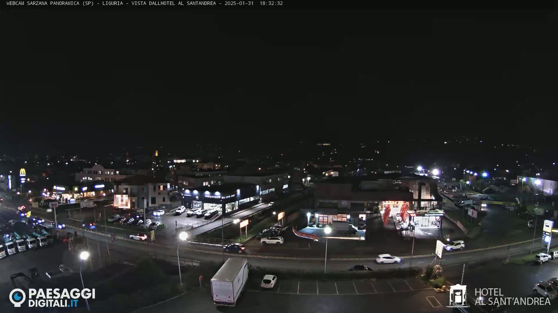 A nighttime aerial view of a town's streets and buildings, showing cars and trucks, illuminated by streetlights and building lights.