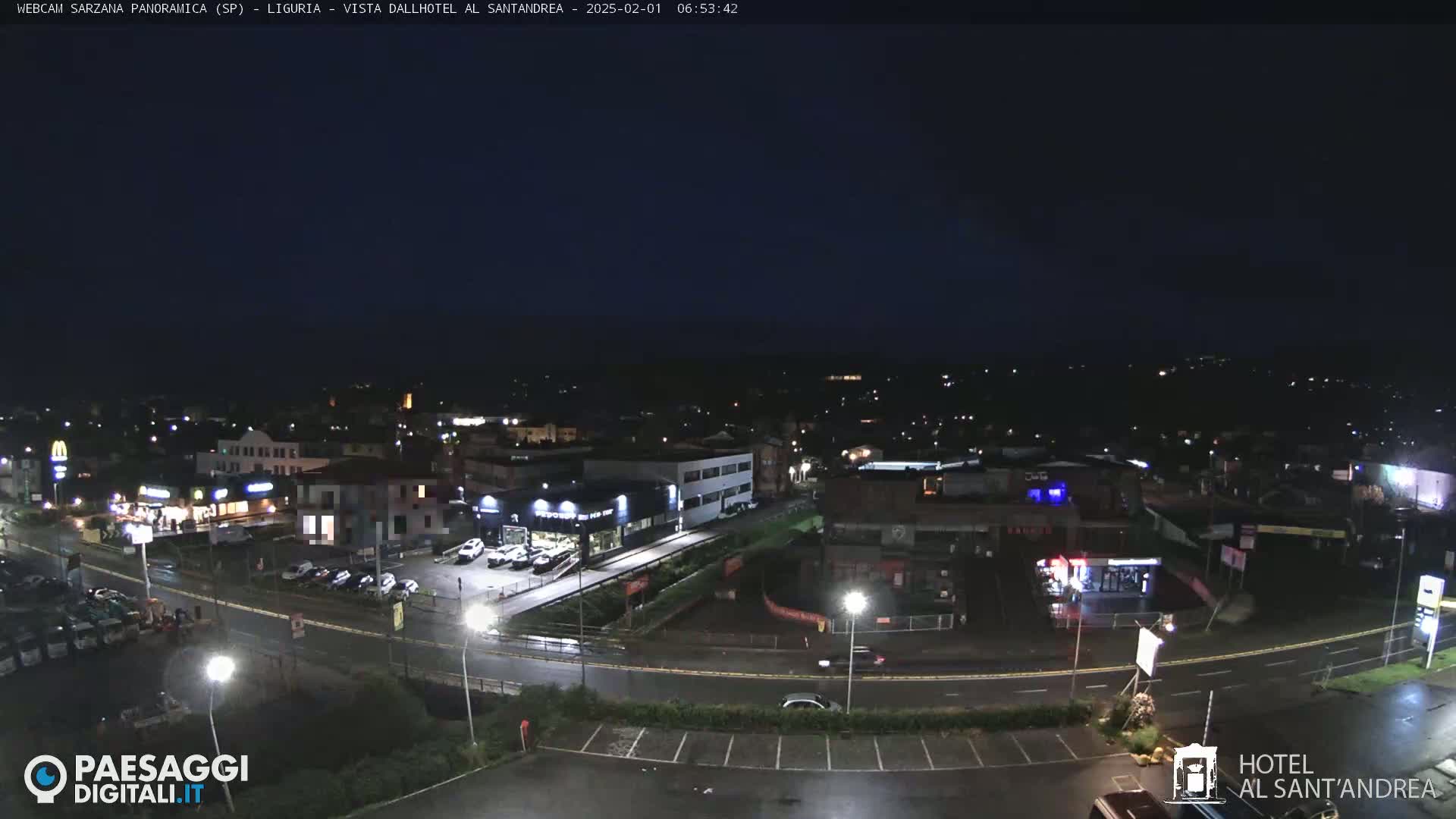 A nighttime, slightly wet view of a town with illuminated buildings and roads.