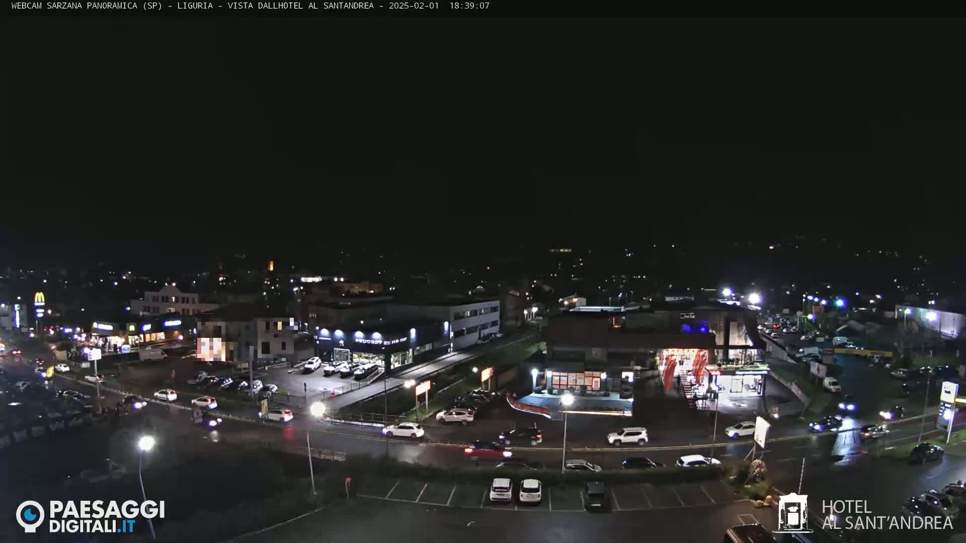 A nighttime, aerial view of a town's streets and businesses, with cars driving on wet roads under a clear, dark sky.