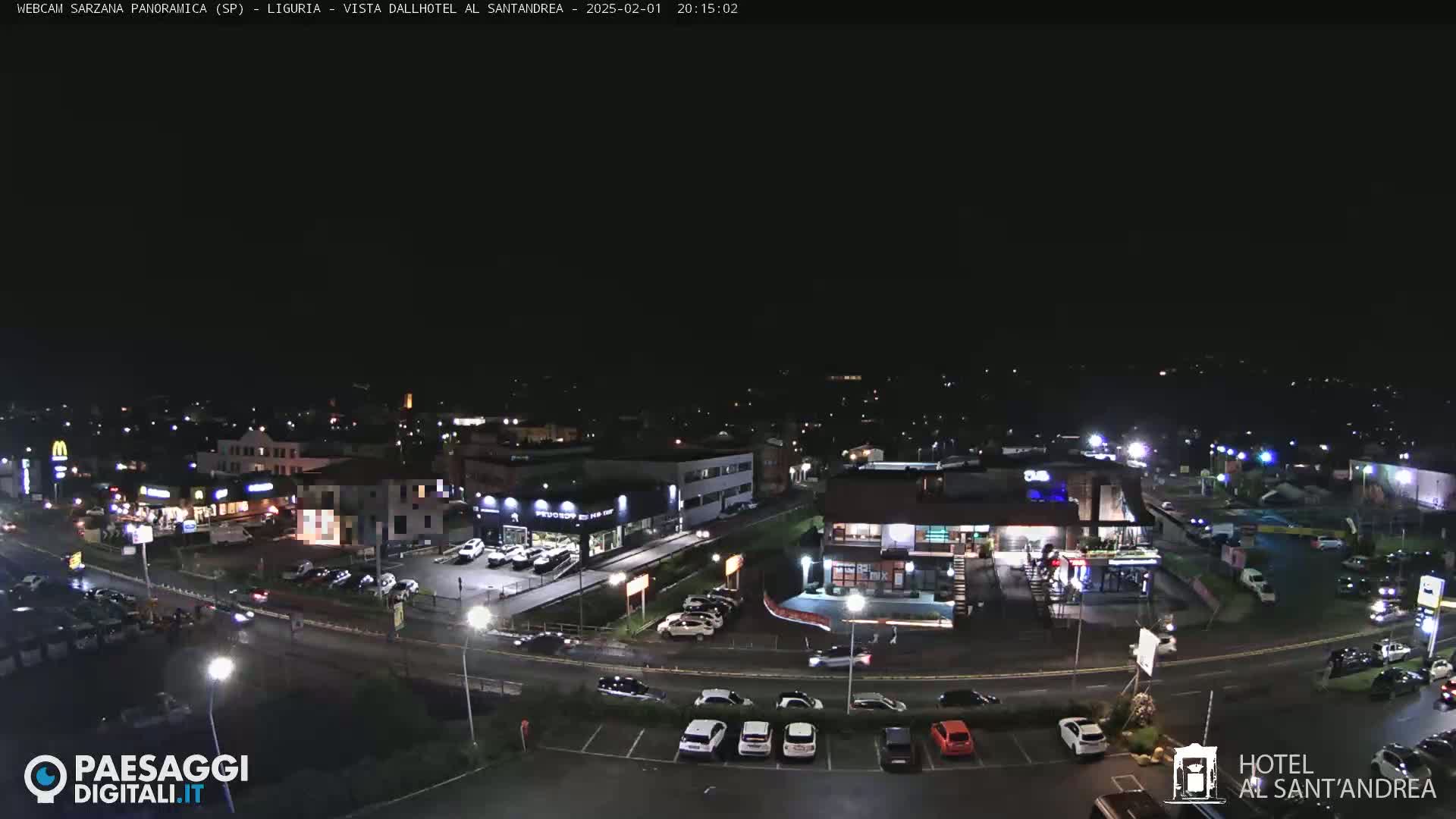 A nighttime aerial view of a town's street scene with several buildings, cars, and parking lots illuminated under a clear, dark sky.
