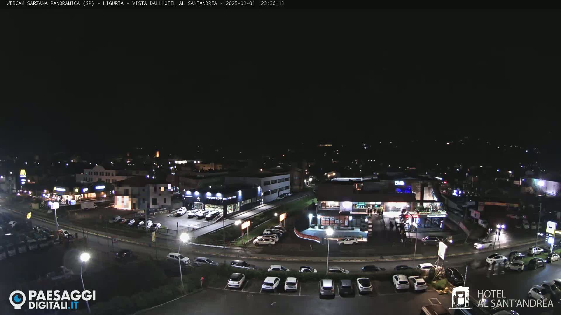 A nighttime aerial view of a town with streets, buildings, parking lots, and cars, under clear, dark skies.