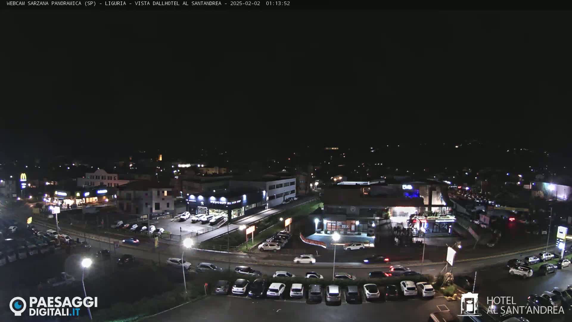 A nighttime aerial view of a town with illuminated buildings, roads, and parked cars under a clear, dark sky.