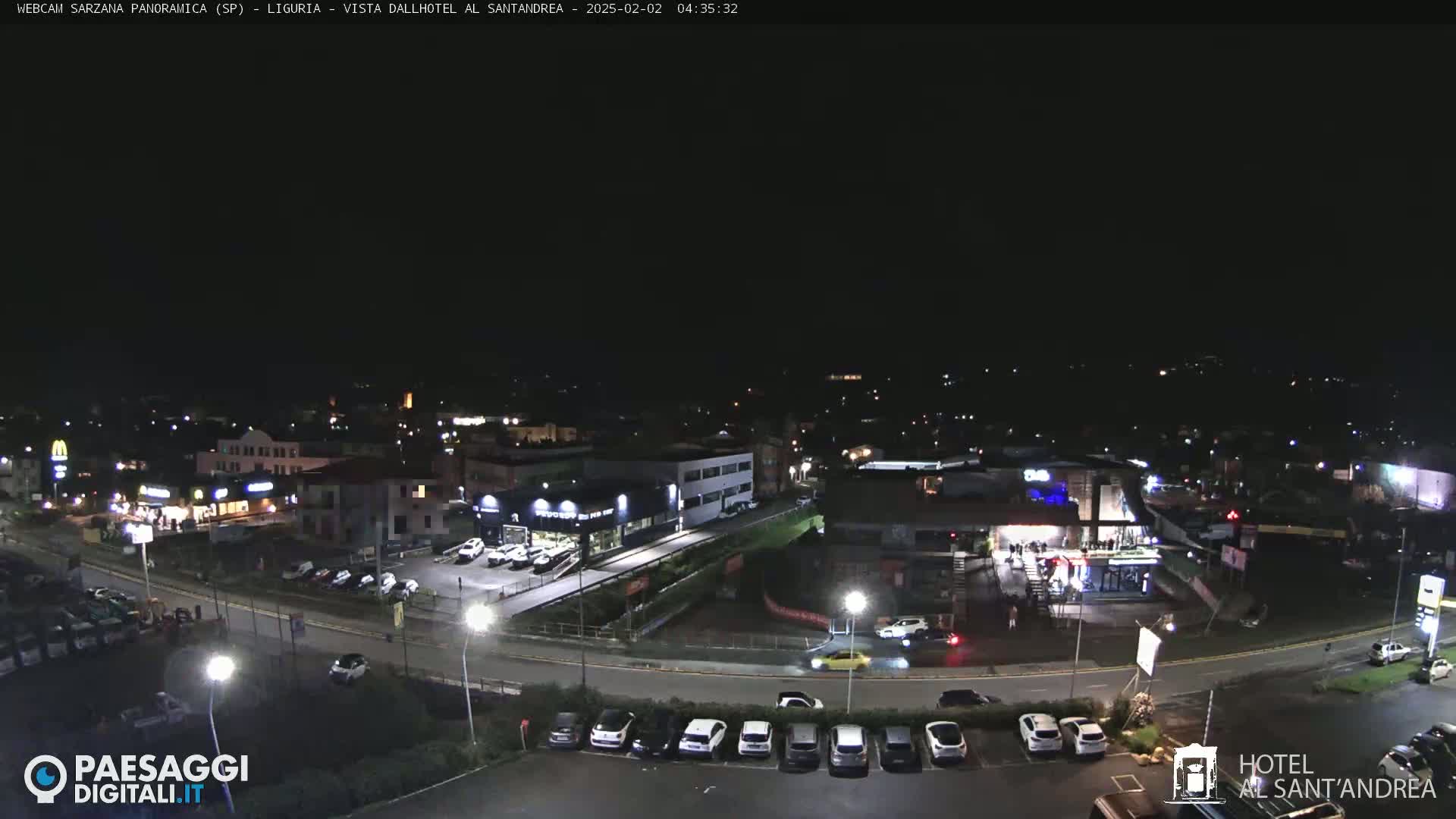 A nighttime, high-angle view of a town with illuminated buildings, roads, and parked cars under a clear, dark sky.