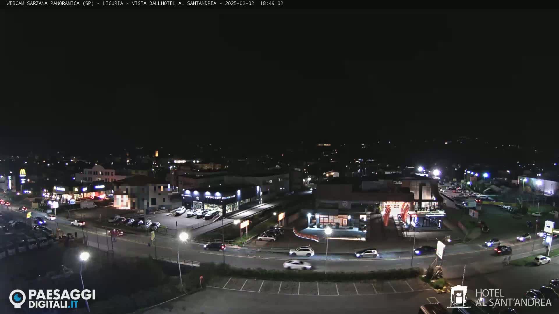 A nighttime aerial view of a town's streets and buildings, showing cars on roads and lit-up businesses.