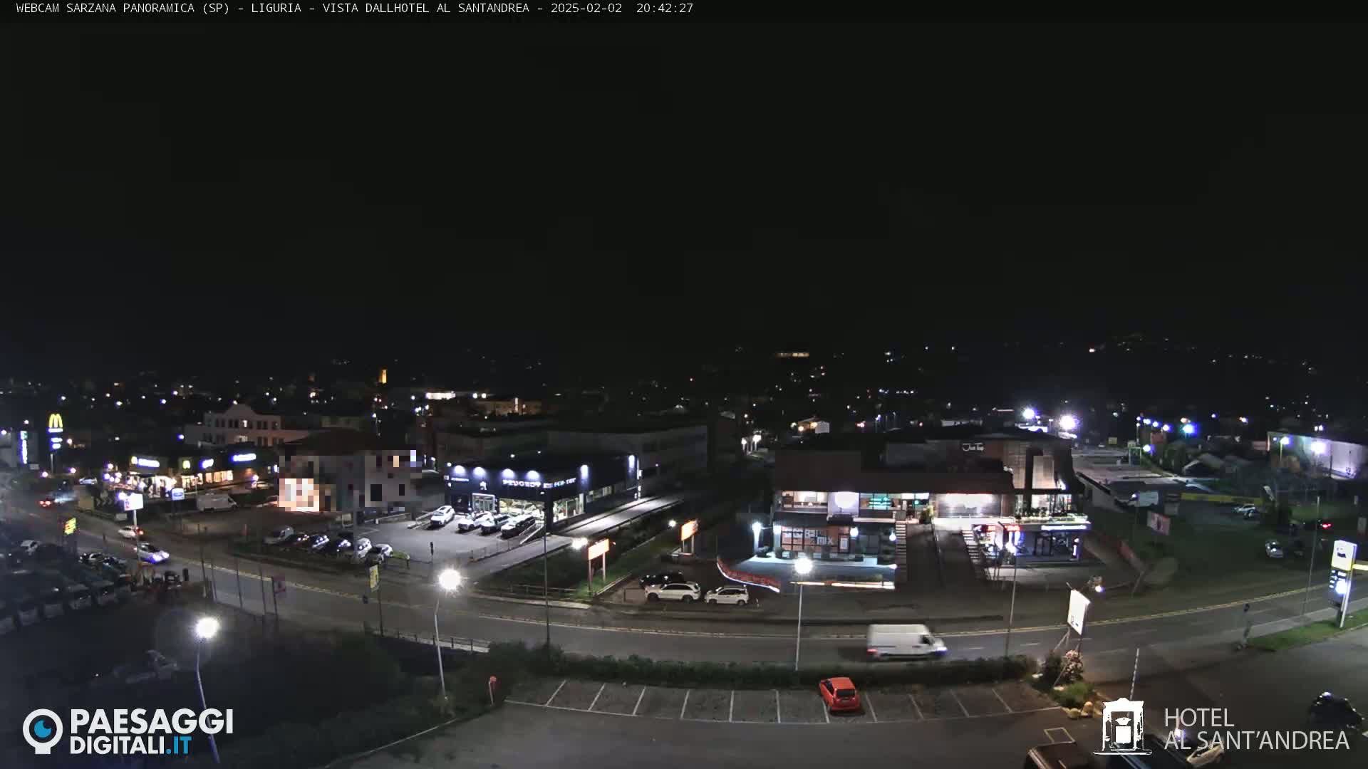 A nighttime, aerial view of a town with illuminated buildings and roads, showing some traffic and parking lots.