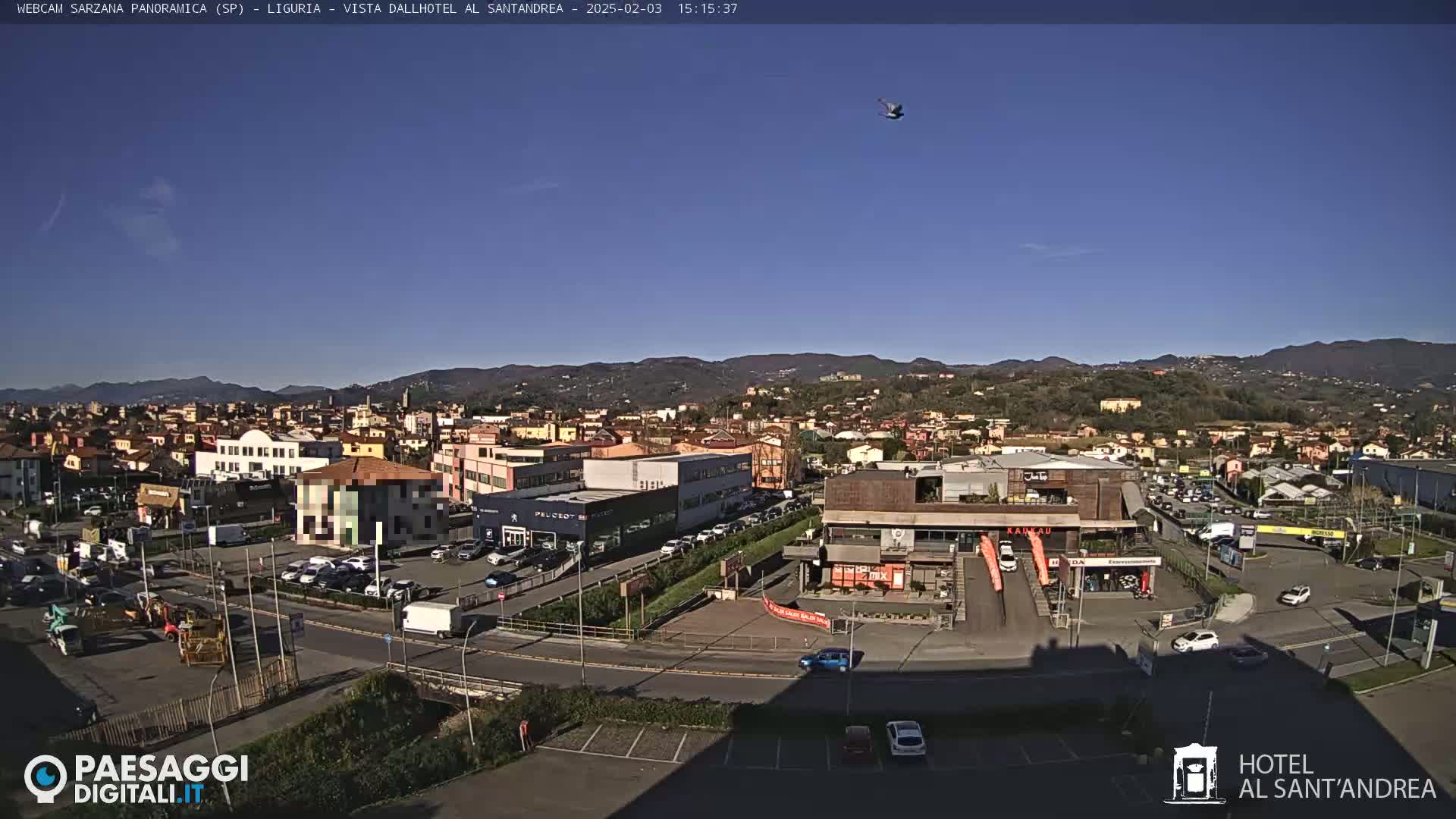 A clear, sunny day reveals a panoramic view of a town nestled amongst hills, featuring buildings, roads, and parked cars.