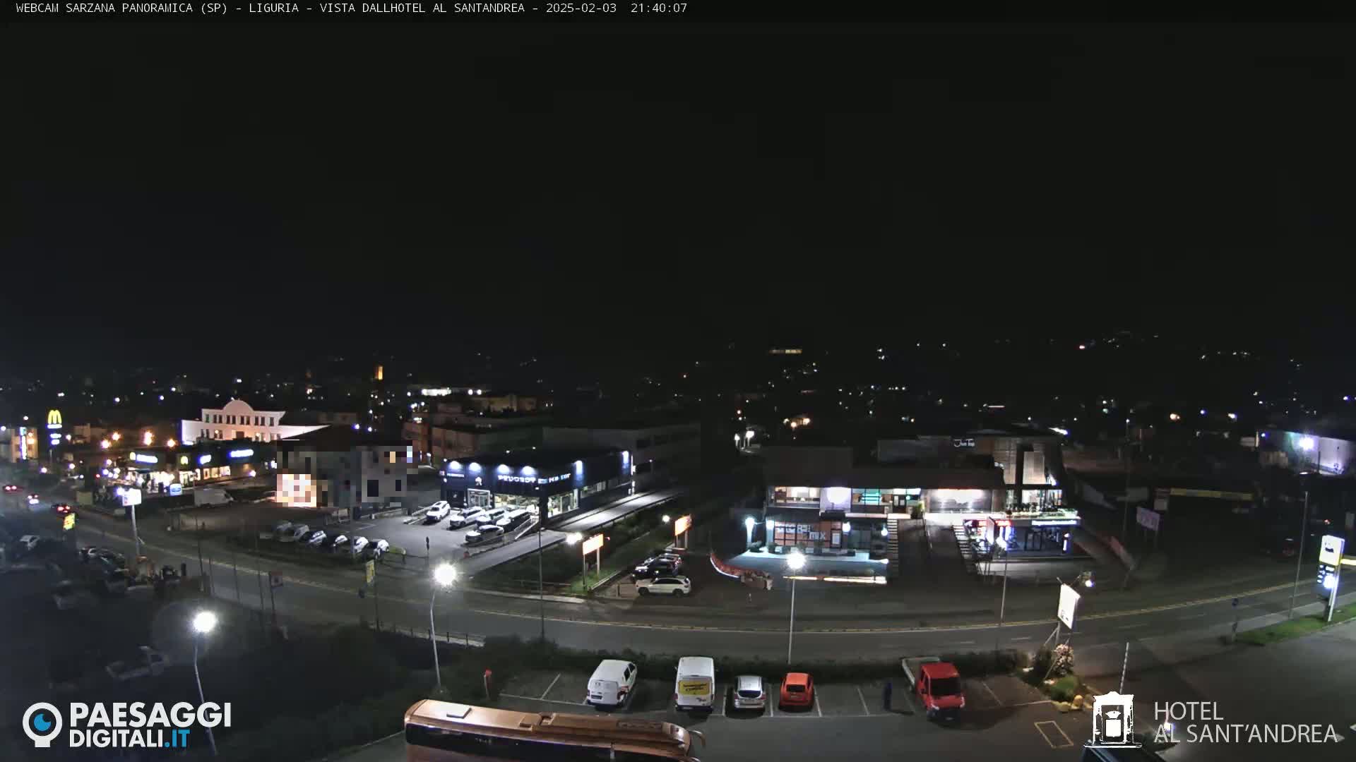 A nighttime, aerial view of a town's street scene showing several buildings, cars in parking lots, and a road with vehicles.