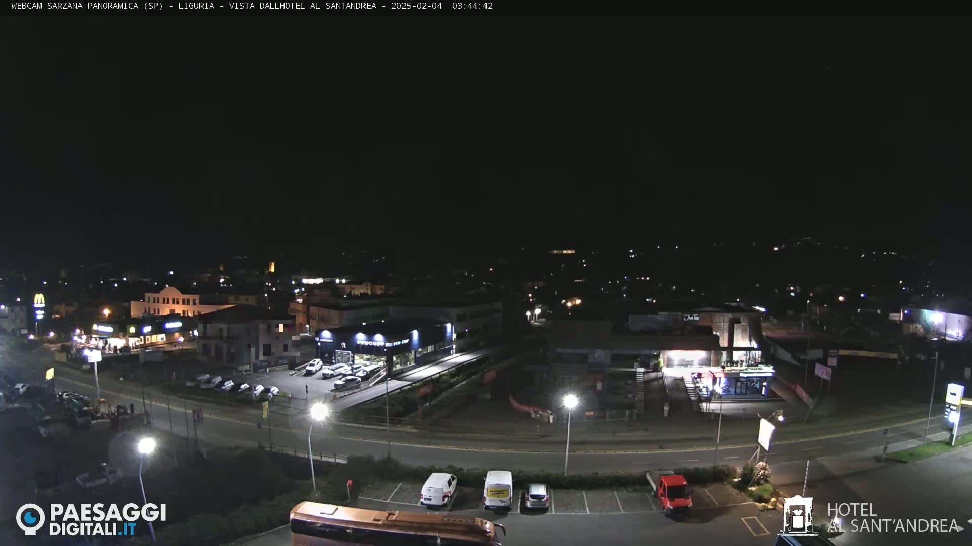 A nighttime, overhead view of a town's outskirts, showing roads, buildings, parked cars, and sparse streetlights.