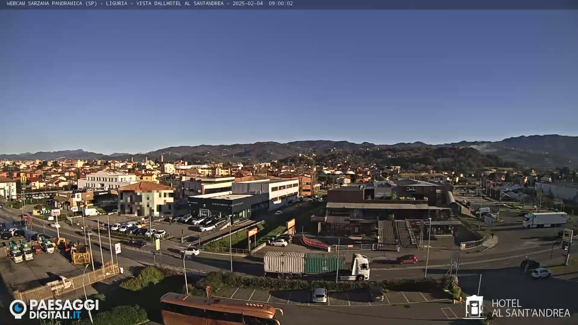A clear, sunny day reveals a sprawling town nestled in a valley, surrounded by distant mountains.