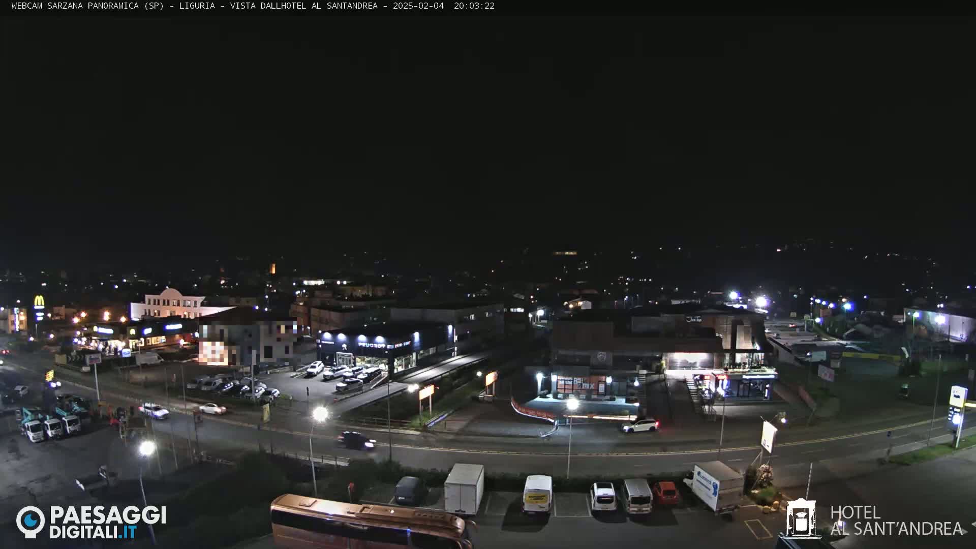 A nighttime aerial view of a town with roads, buildings, and parked cars under a clear, dark sky.