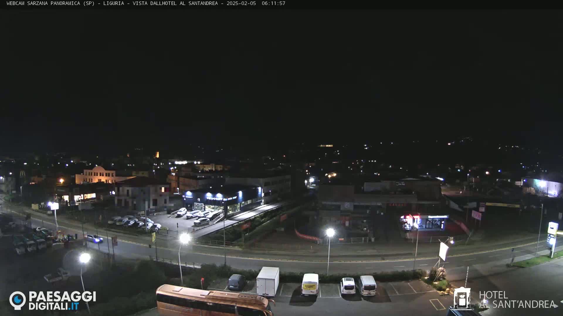 A nighttime, overhead view of a town with roads, buildings, cars, and a bus, under a dark sky.