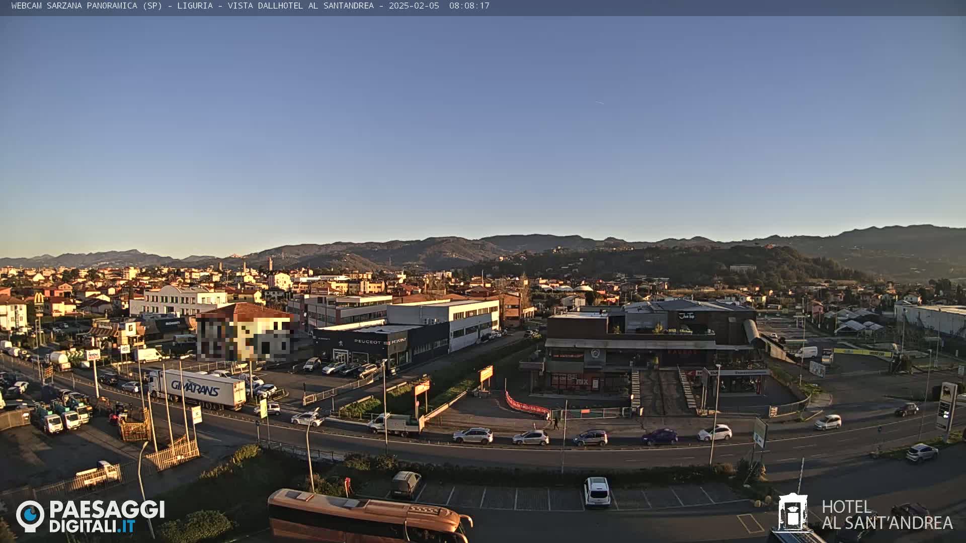 A clear, sunny day reveals a panoramic view of a town nestled in a valley, with mountains in the background and numerous vehicles on roads and in parking lots.