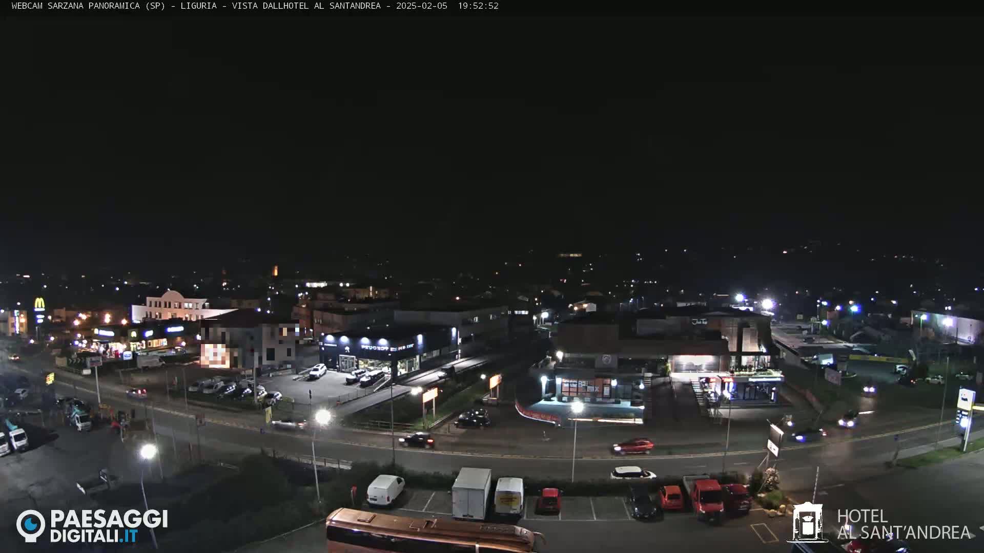 A nighttime, aerial view of a town's road network and buildings, including businesses and a parking lot with cars.