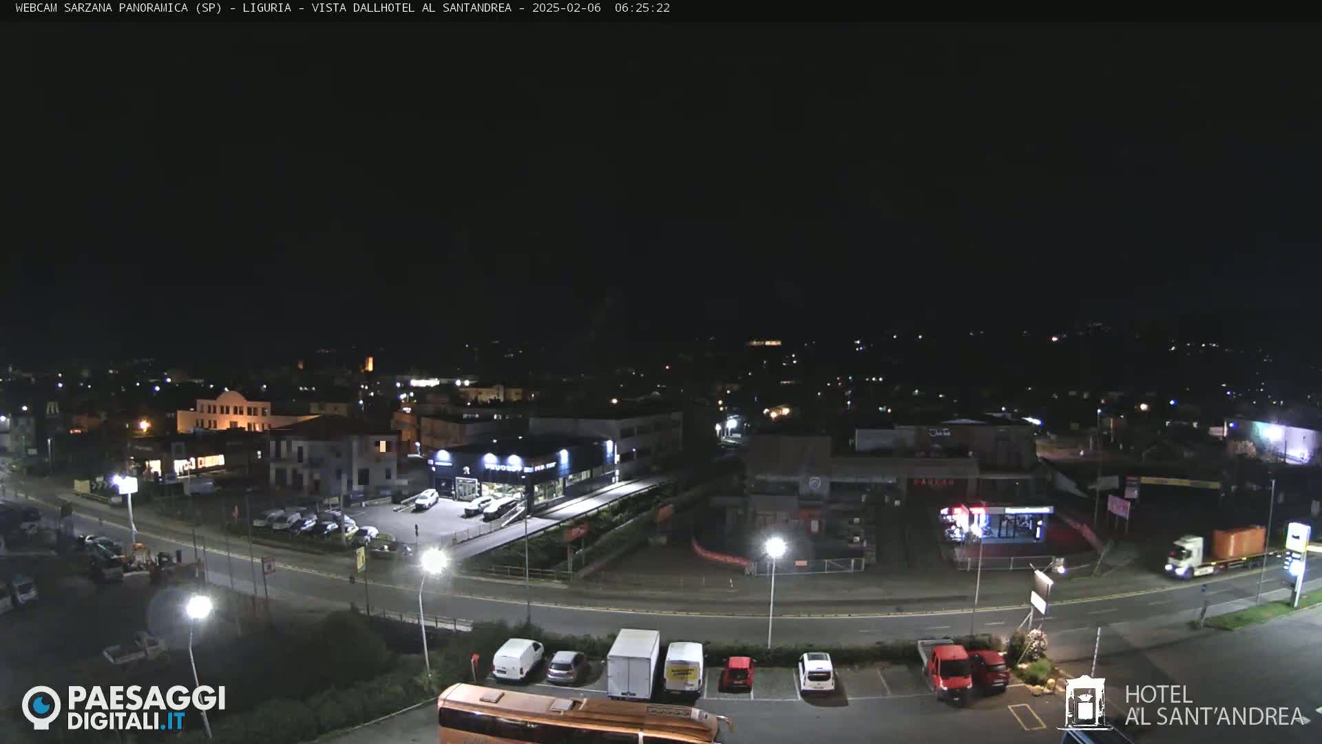 A nighttime aerial view of a town with streets, buildings, cars, and a bus in a parking lot under a clear, dark sky.