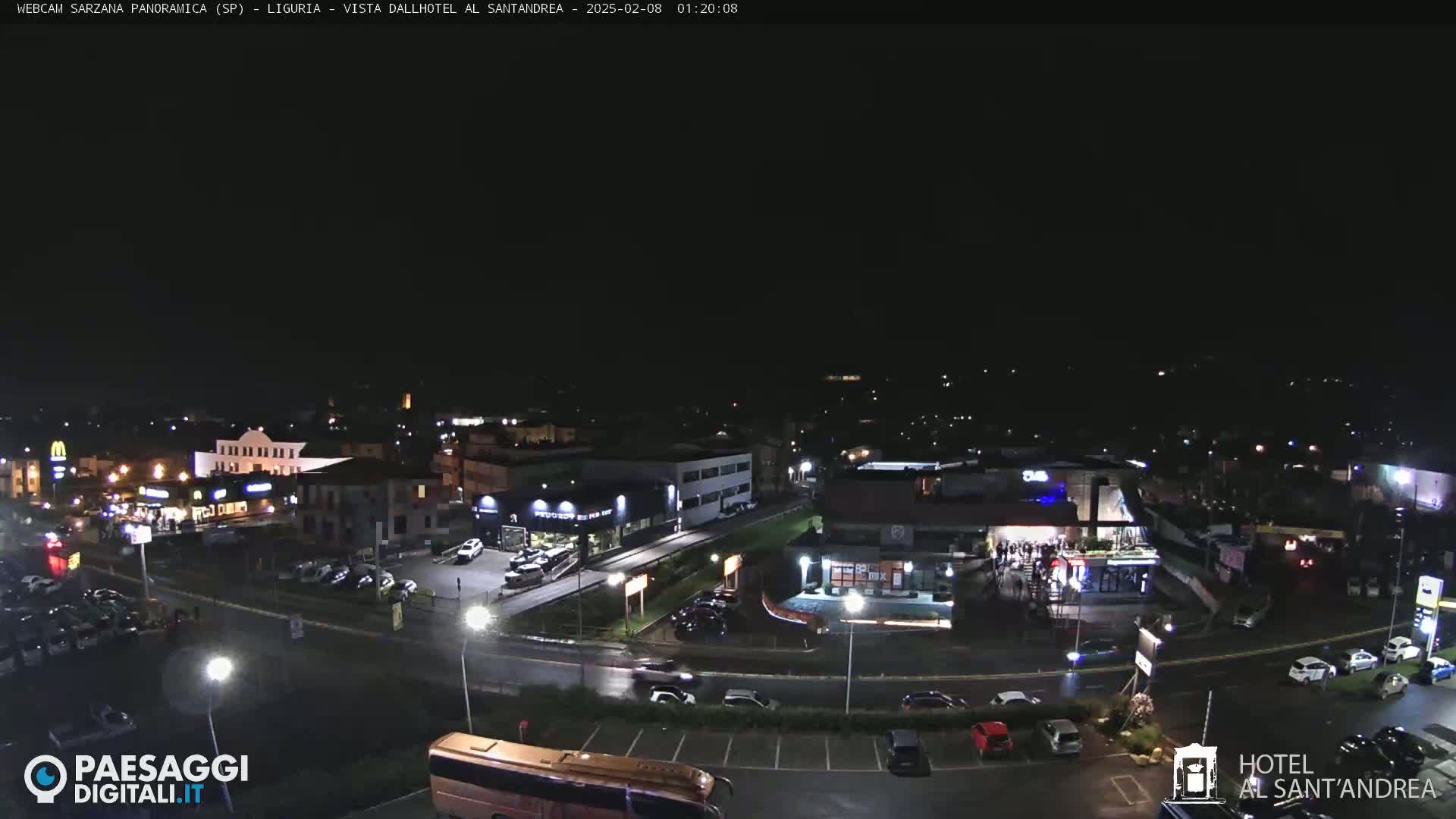 A nighttime aerial view of a town with cars parked in lots surrounding buildings and roads, under a clear, dark sky.