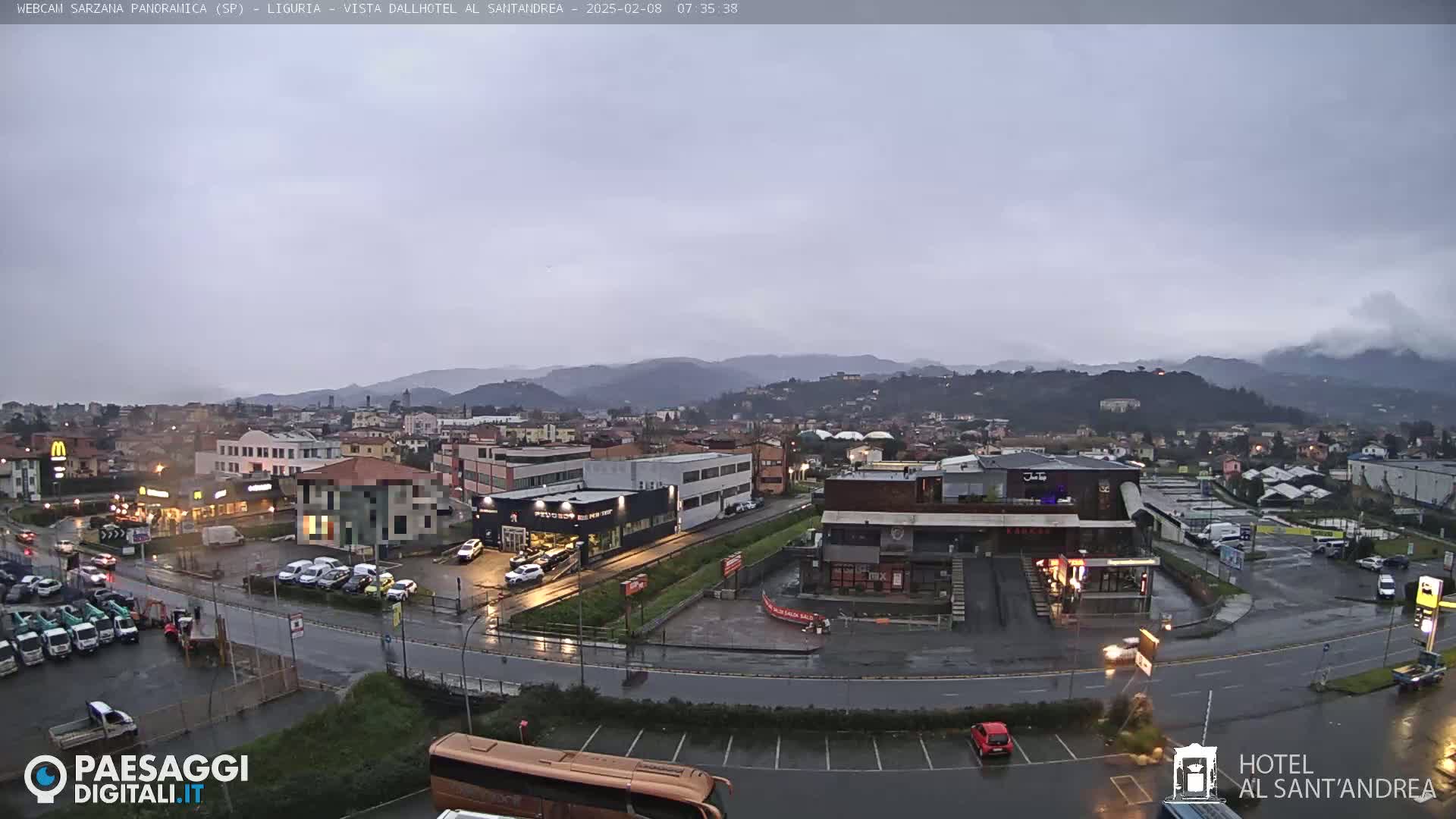 A wet, overcast view of a town nestled in a valley, with mountains in the background and various buildings, including businesses and parking lots, visible in the foreground.