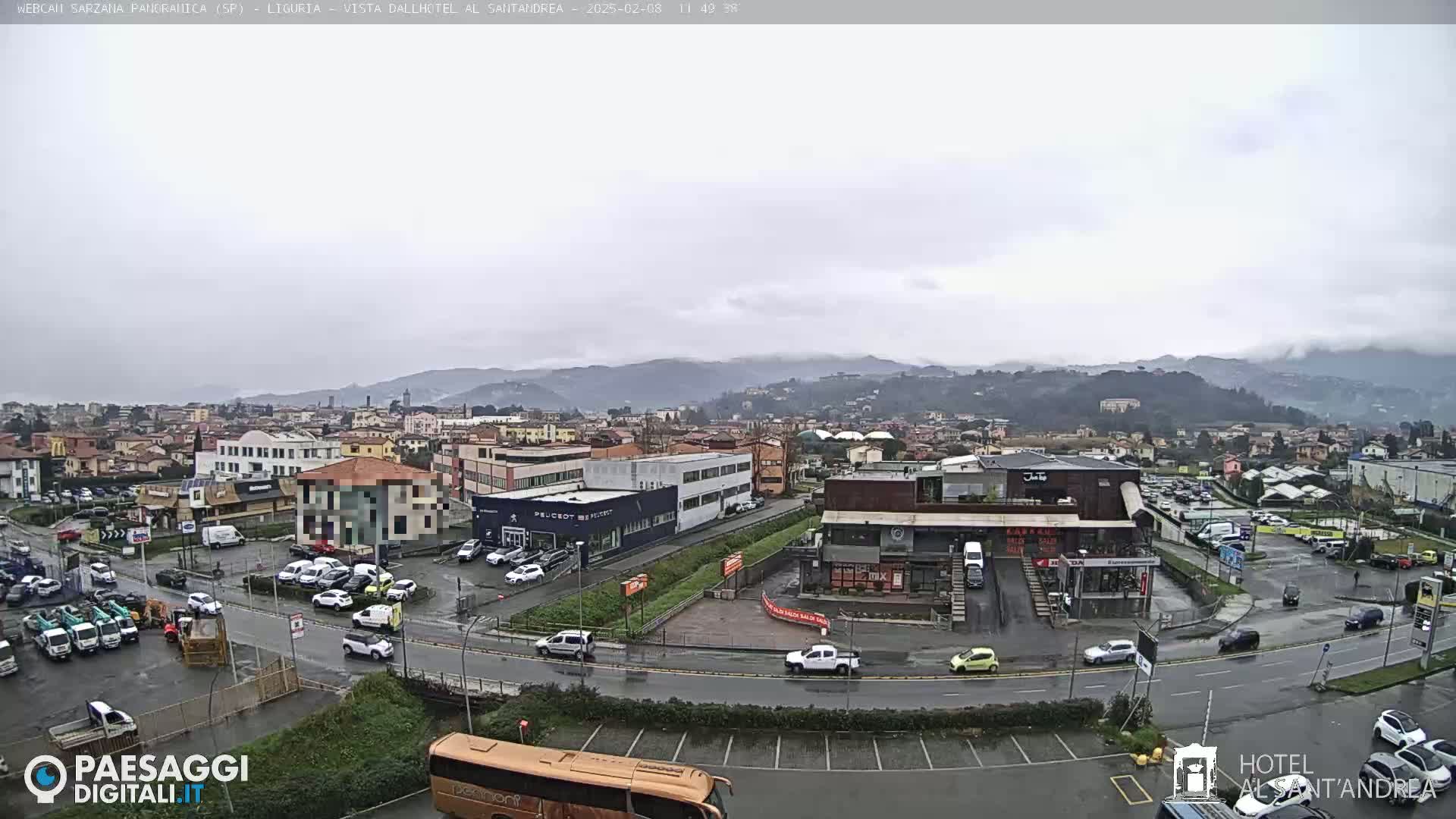 A wide, overcast view of a town and surrounding mountains, with wet roads and numerous cars parked in lots.
