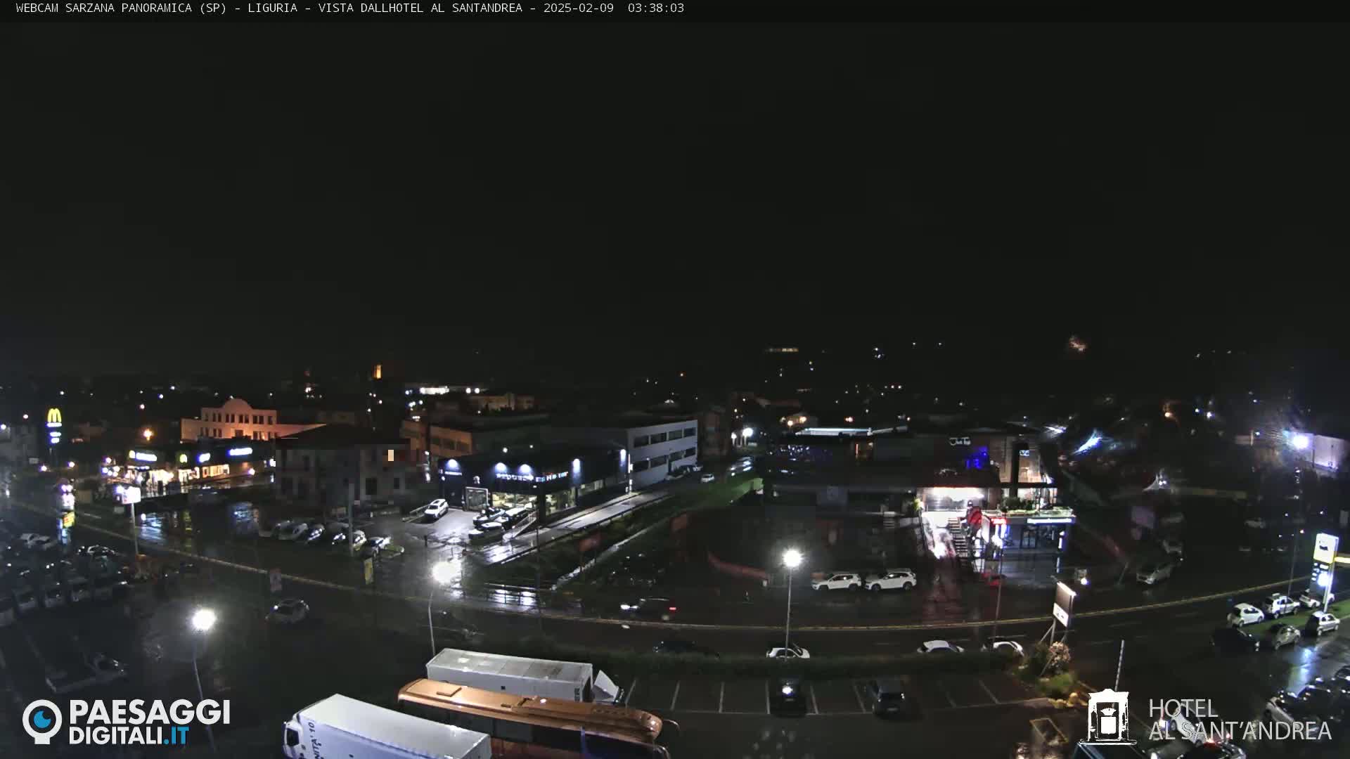A nighttime, wet view of a town with buildings, roads, and parked cars.