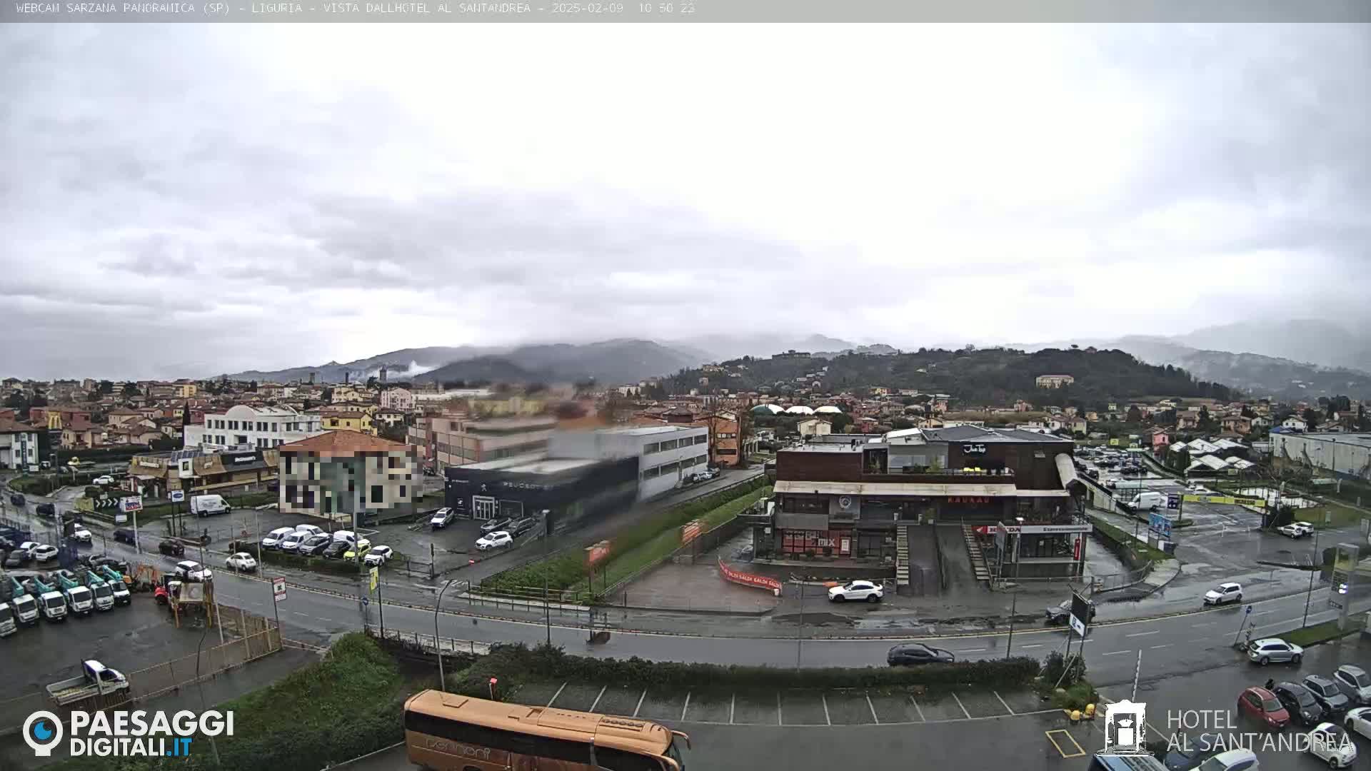 A rain-soaked town sprawls beneath a cloudy sky, with distant hills shrouded in mist.