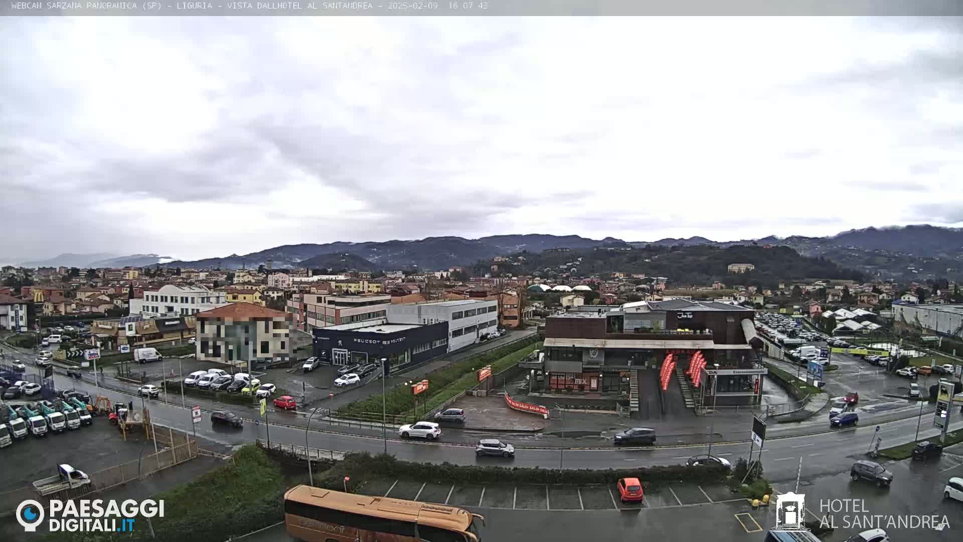 A wide, overcast view of a town situated in a valley, with cars parked in lots and driving on wet roads in front of various buildings, including restaurants and dealerships.