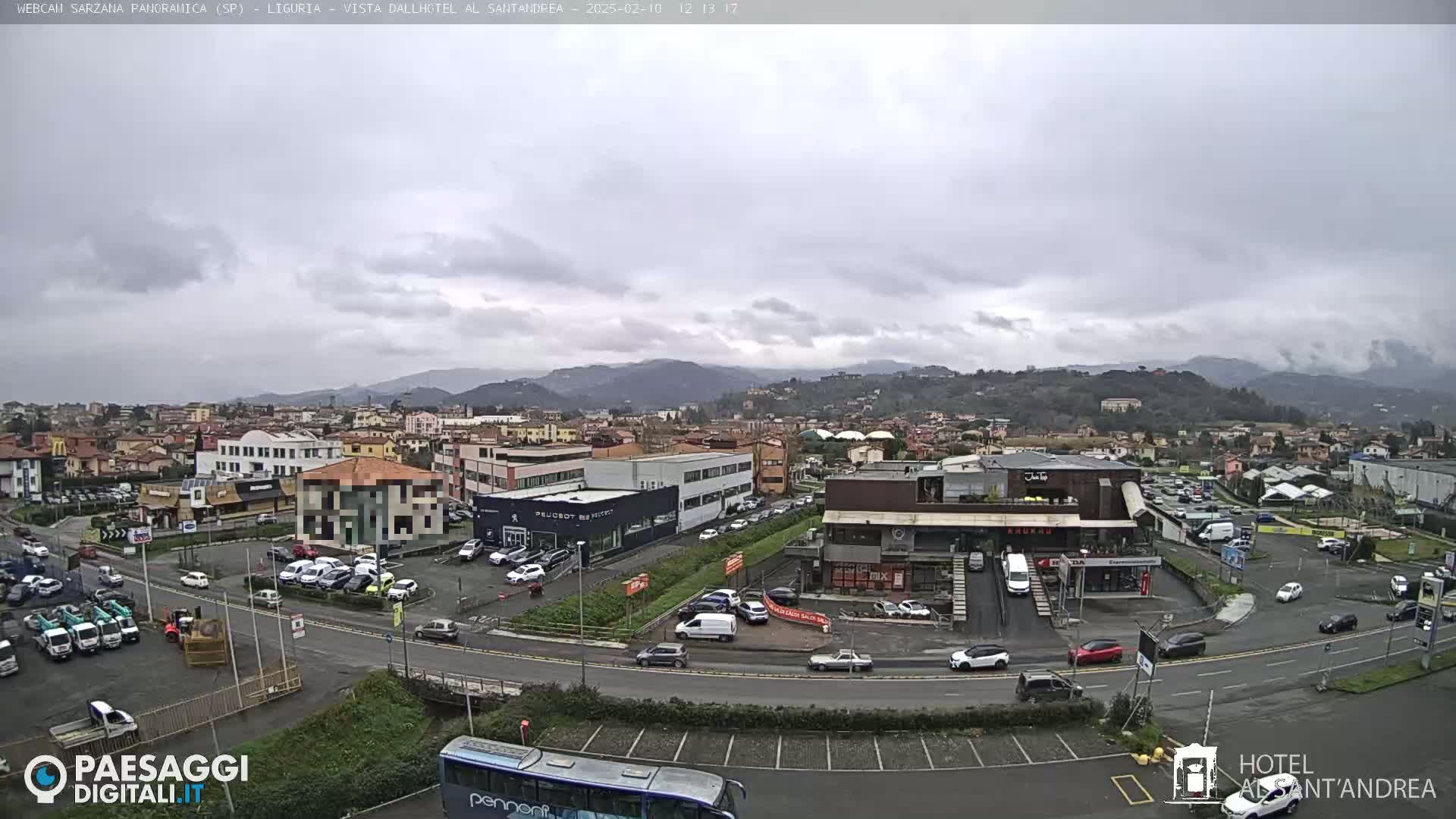 A wide shot of a town under an overcast sky shows several buildings, parking lots filled with cars, and a bus at a roadside.