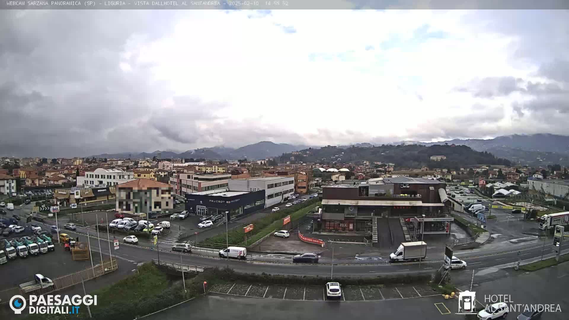 A cloudy day reveals a sprawling town nestled among low hills, with a busy roadway and numerous parked cars visible.