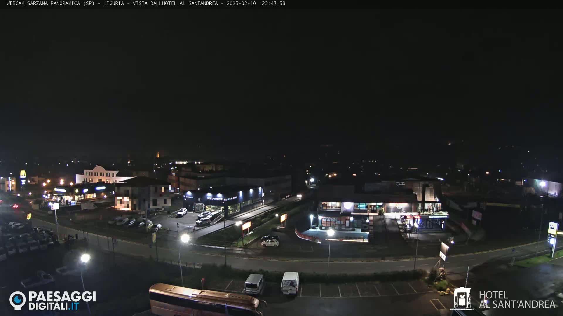 A nighttime aerial view of a town's commercial district, showing streets, parked cars, and illuminated buildings.