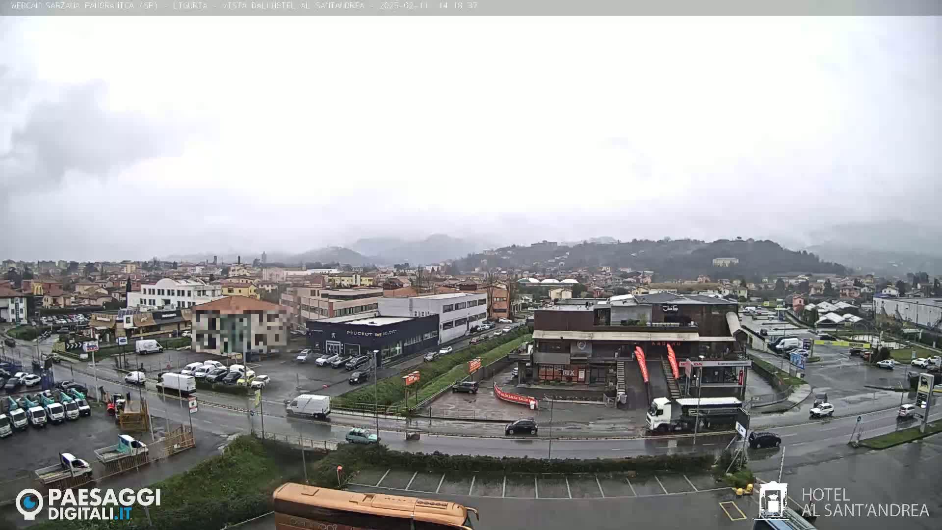 A rain-covered view of a town with buildings, cars, and a large parking lot, set against a backdrop of misty hills.