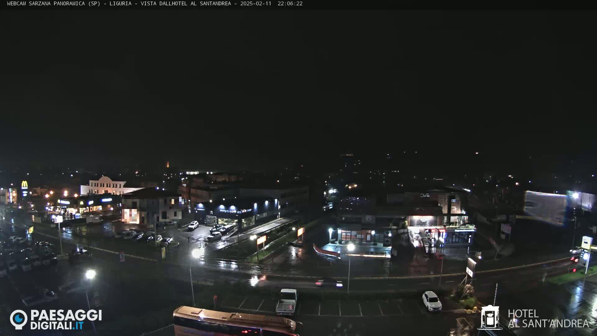A nighttime, rain-slicked parking lot and roadway scene shows several buildings, vehicles, and some streetlights.