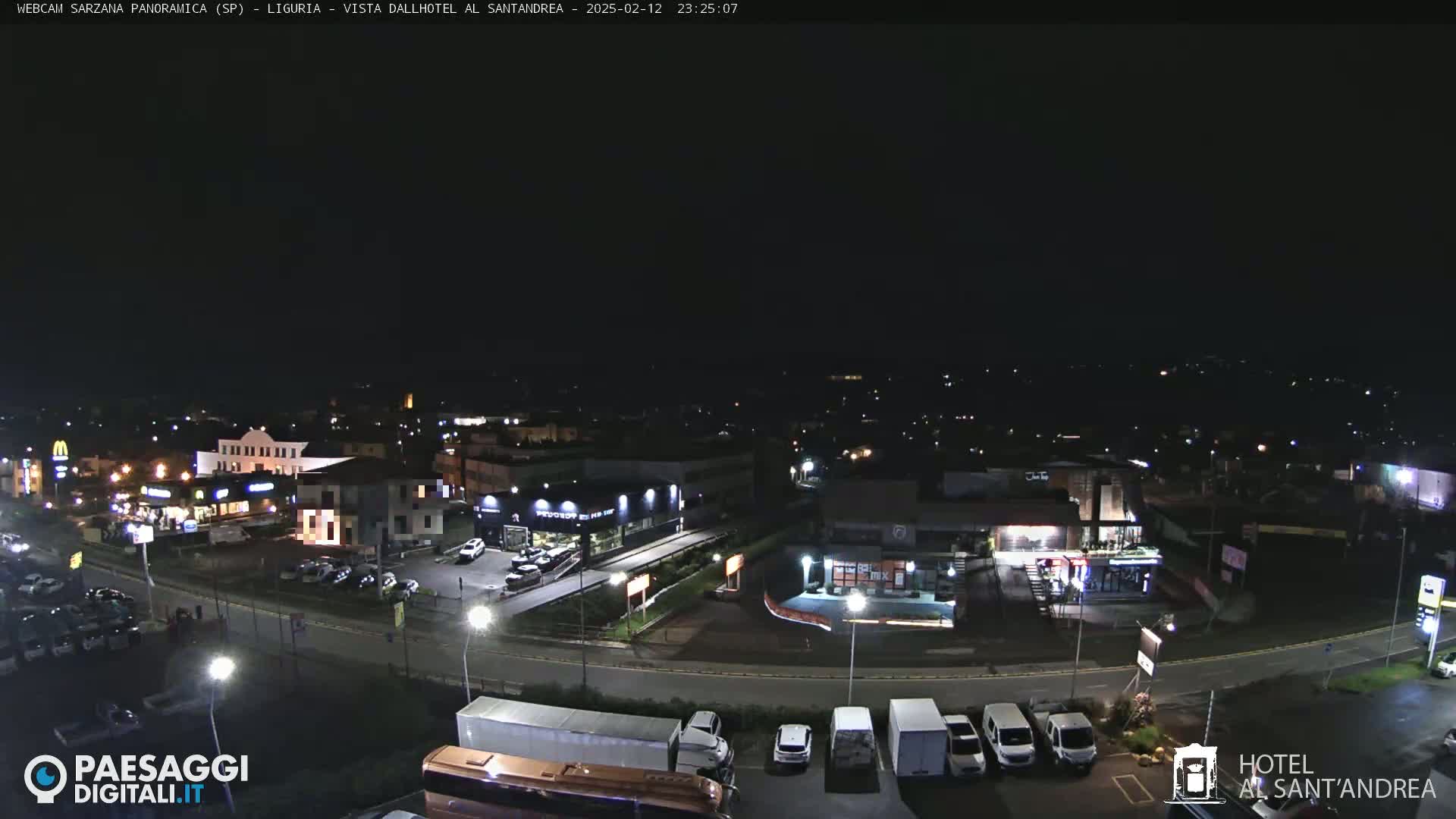 A nighttime aerial view of a town with illuminated buildings and vehicles parked along roads and in parking lots, under a clear, dark sky.