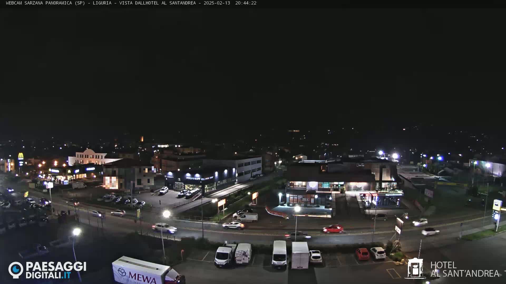 A nighttime, high-angle view of a town's streets and parking lots with cars and buildings illuminated by streetlights.