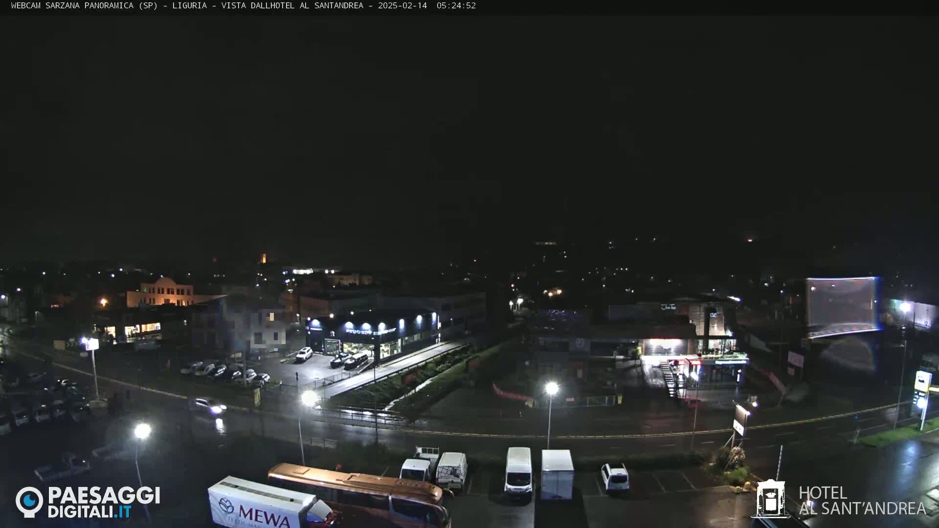 A nighttime, wet aerial view of a parking lot, roadways, and buildings with streetlights illuminating the scene.